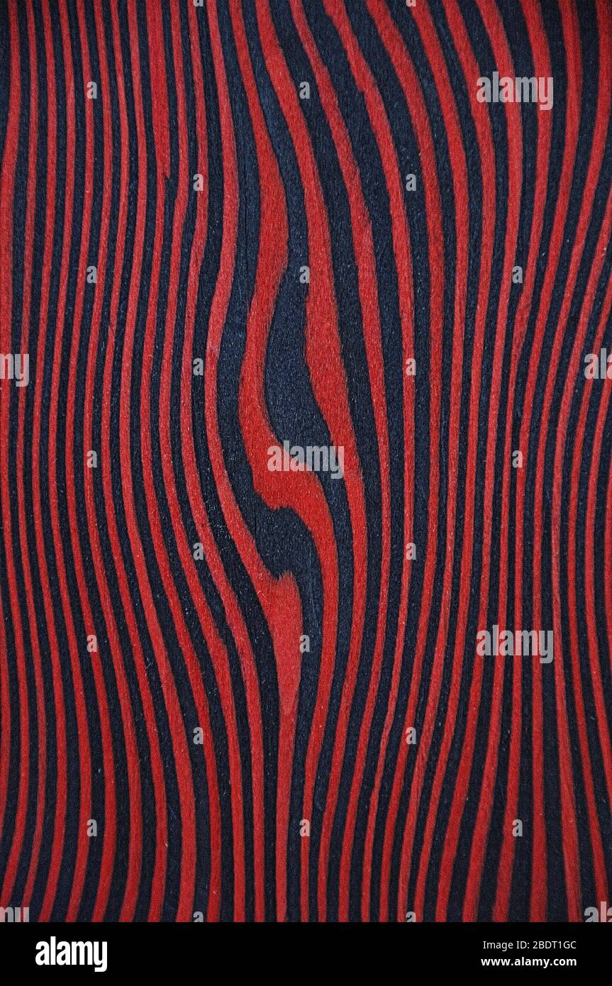 Die Texturen eines exotischen Holzes. Roter Hintergrund mit schwarzen Streifen. In der Mitte des Gyrus. Stockfoto
