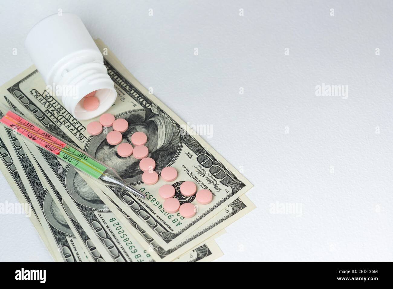 Tabletten sind in US-Dollar, ein medizinisches Thermometer verstreut. Verluste durch Behandlung und Quarantäne der COVID-19-Coronavirus-Pandemie. Kopierbereich Stockfoto