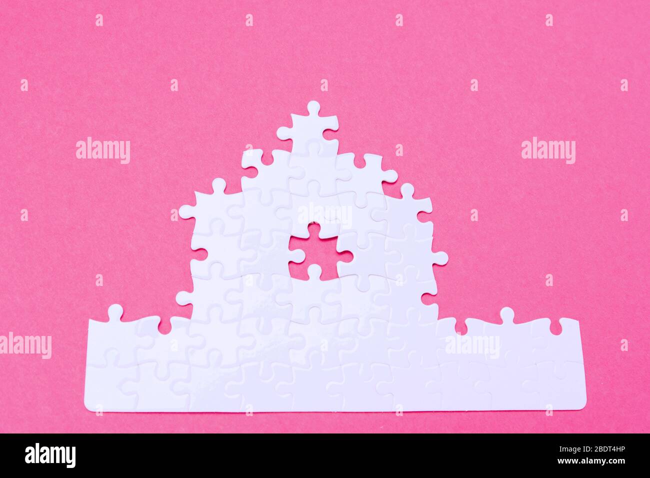 Weißes Puzzle. Haus Form Puzzle. Das Konzept der Miete, Hypothek. Rosa Hintergrund. Draufsicht Stockfoto
