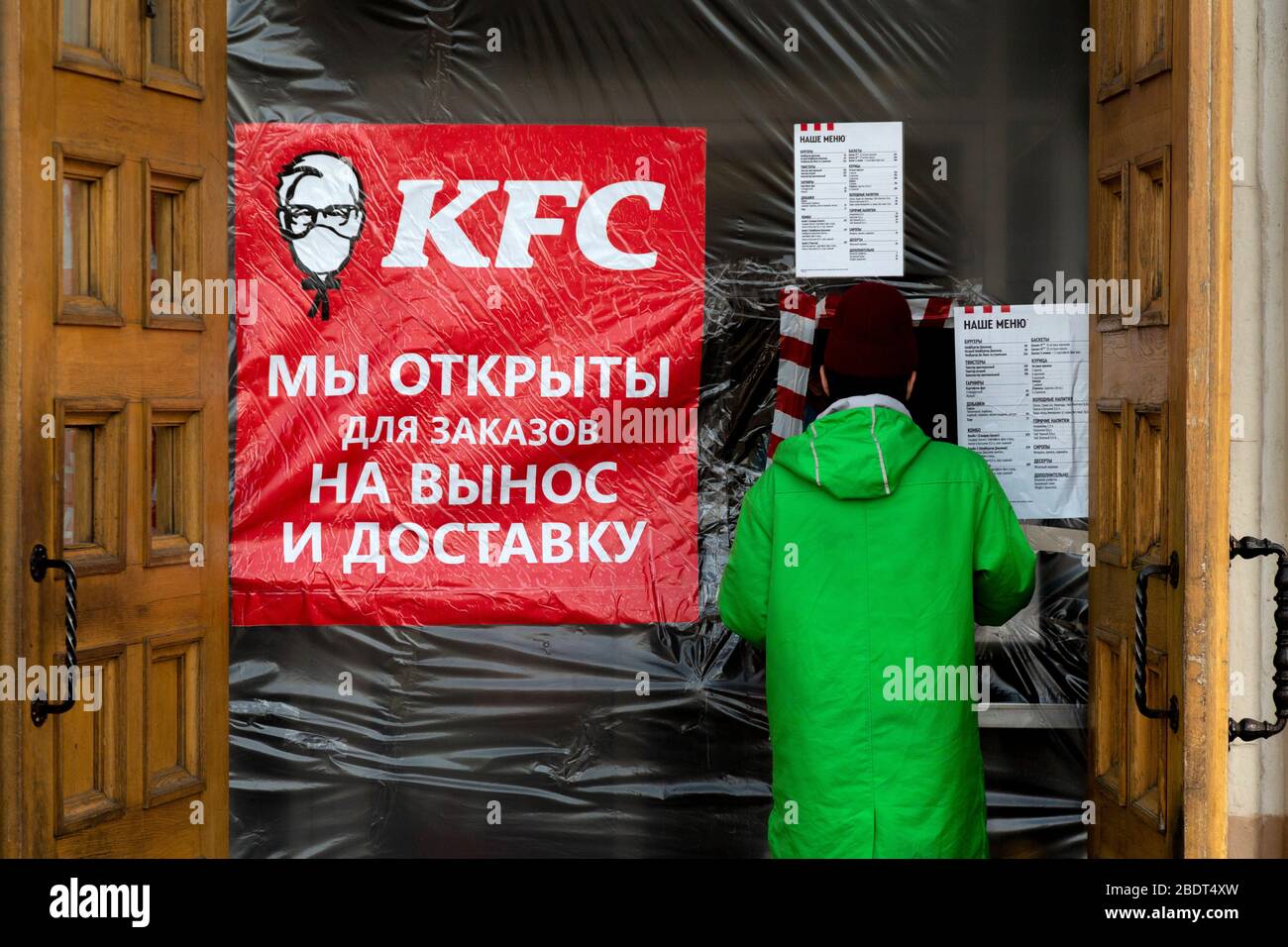 Moskau, Russland. April 2020. Ein Kurier des Lebensmittelzulieferdienstes "Delivery Club" kauft während der Novelkoronavirus COVID-19-Epidemie in Russland im KFC-Restaurant auf dem Komsomolskaya-Platz im Zentrum Moskaus Lebensmittel ein. Auf dem Banner vor dem KFC-Restaurant steht: "Wir sind offen zum Mitnehmen". KFC änderte das Firmenlogo und fügte eine medizinische Maske hinzu Stockfoto