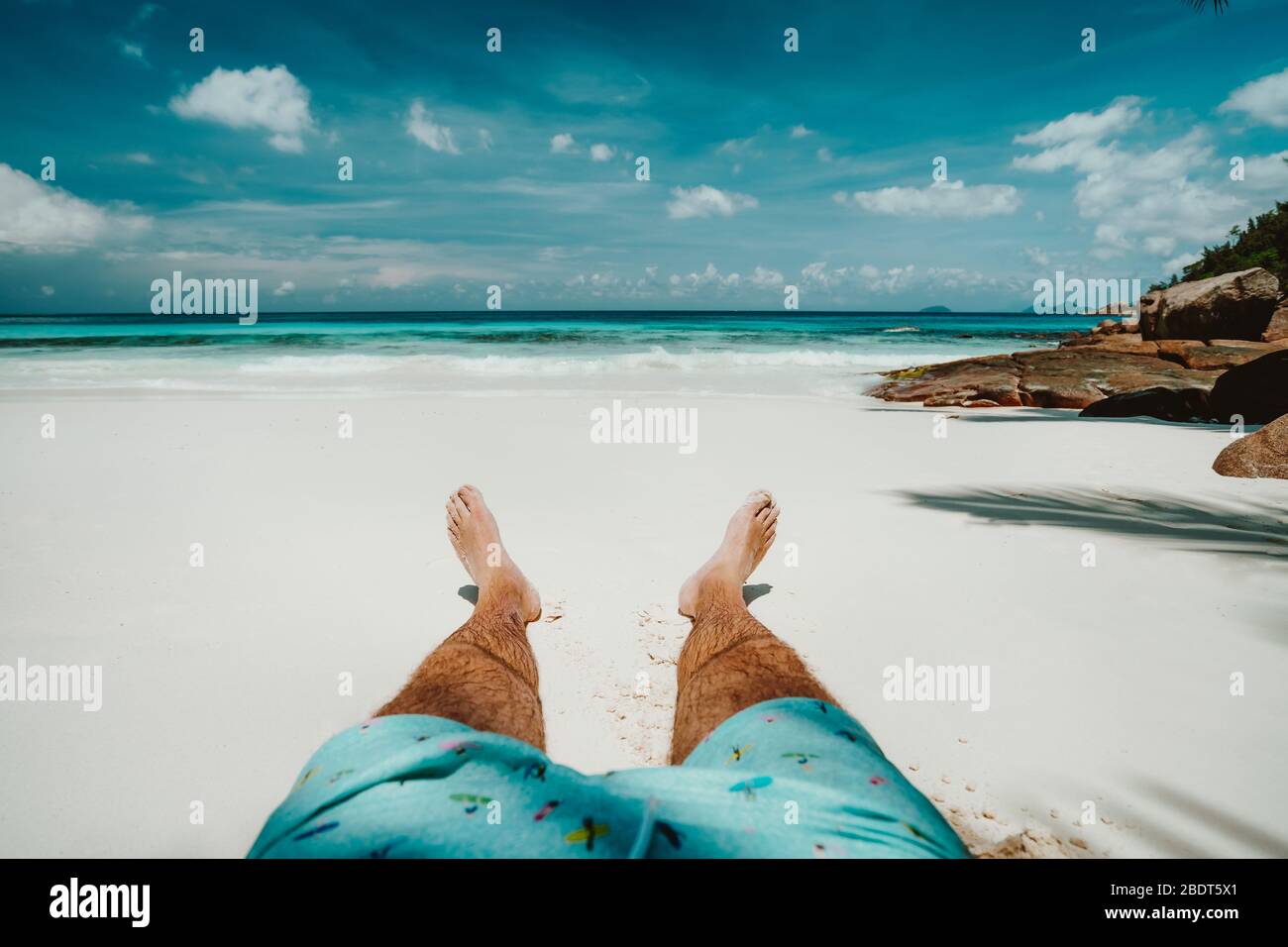 Männer in Badeshorts, die sich auf dem weißen Sandstrand mit wunderschönem Blick auf die Lagune des blauen Ozeans ausruhen. Stockfoto