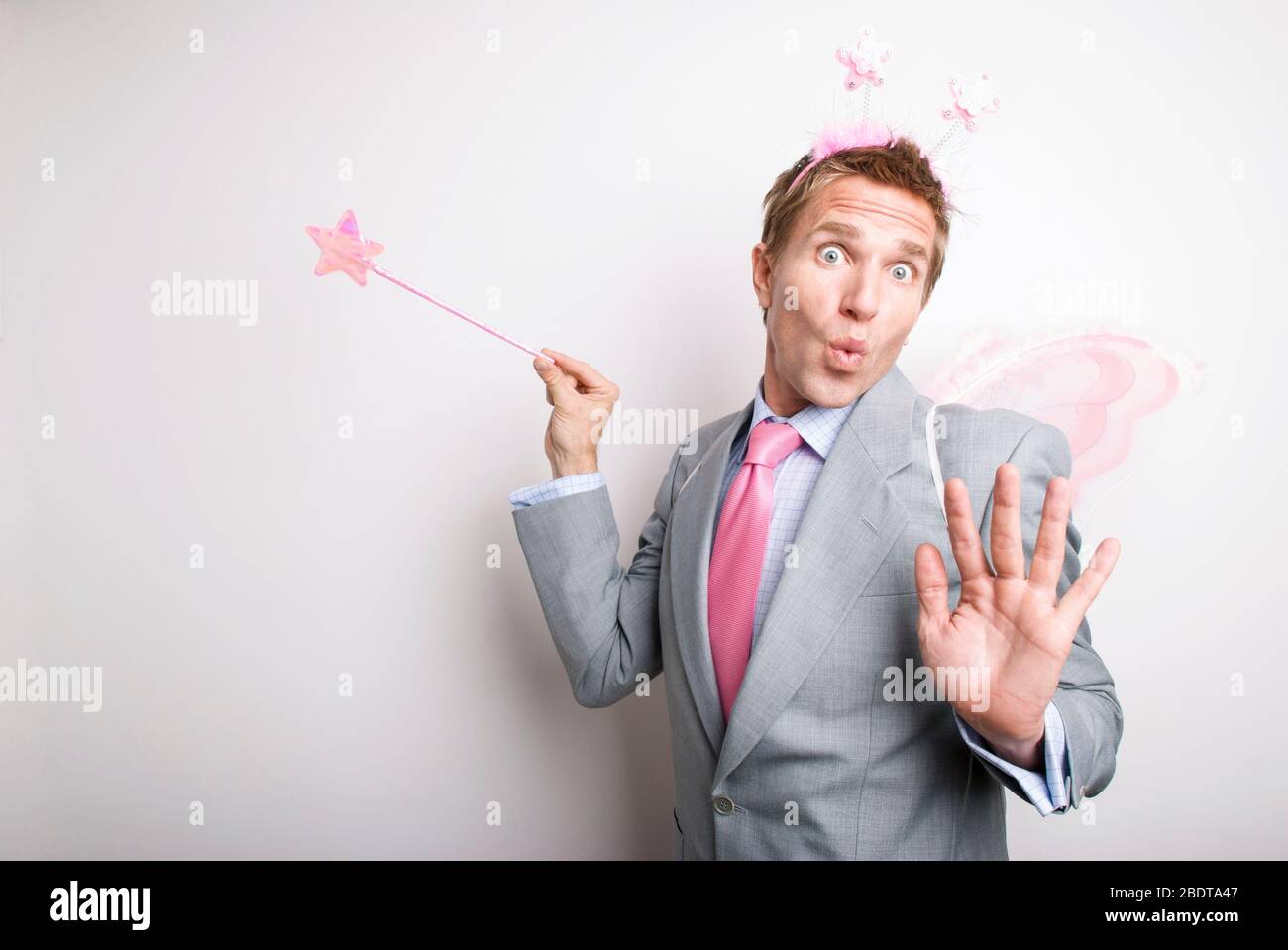 Fee Geschäftsmann winkt ein rosa glitzernden Stern Zauberstab Gewährung eines Wunsches mit einem lustigen Ausdruck auf seinem Gesicht Stockfoto