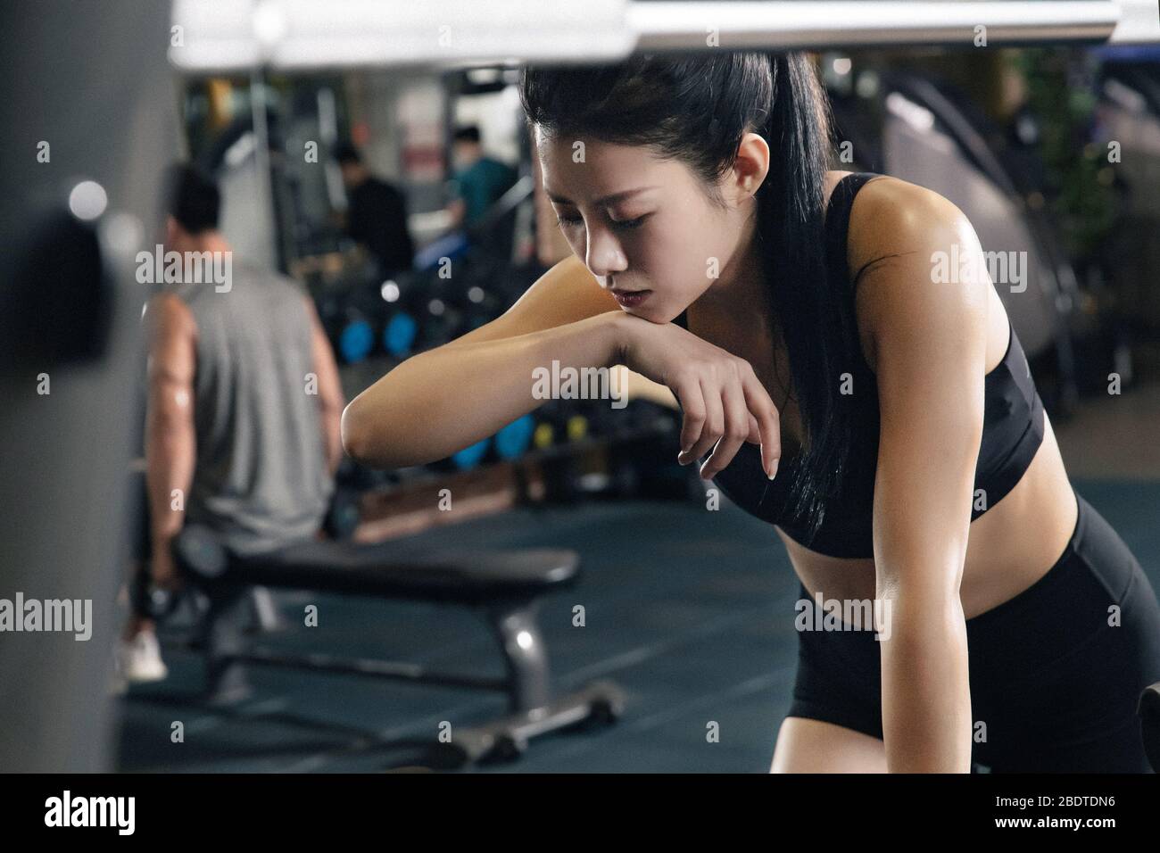 Junge Frau lügt, um den Schweiß auf den Fitnessgeräten abzuwischen Stockfoto