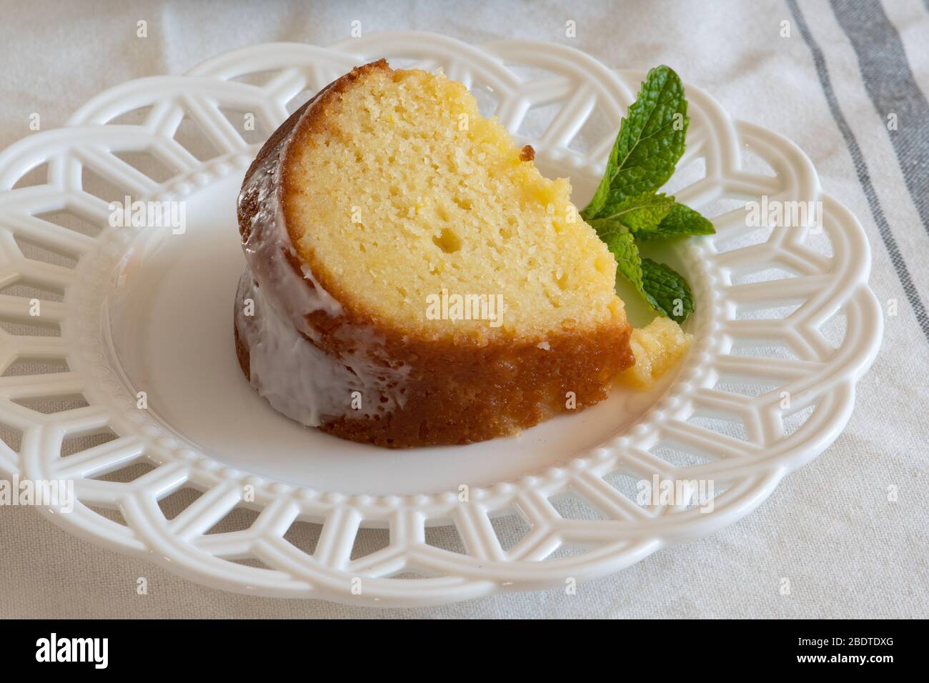 Eine Scheibe Feuchte Zitronenrikowatte-Kuchen auf einem weißen dekorativen Teller mit einer Minzblattgarnitur. Stockfoto
