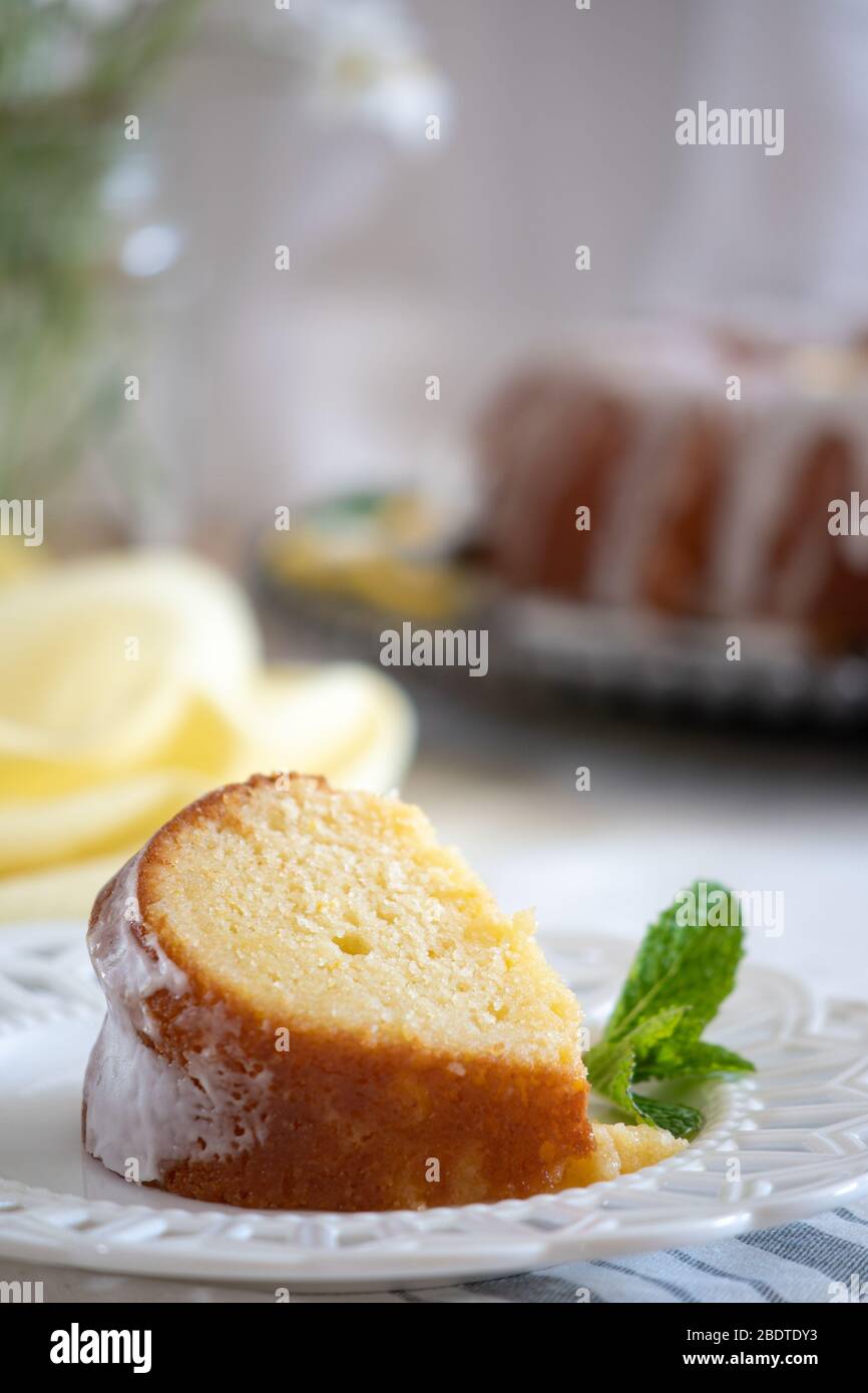 Eine Scheibe Feuchte Zitronenrikowatte-Kuchen auf einem weißen dekorativen Teller mit einer Minzblattgarnitur. Stockfoto