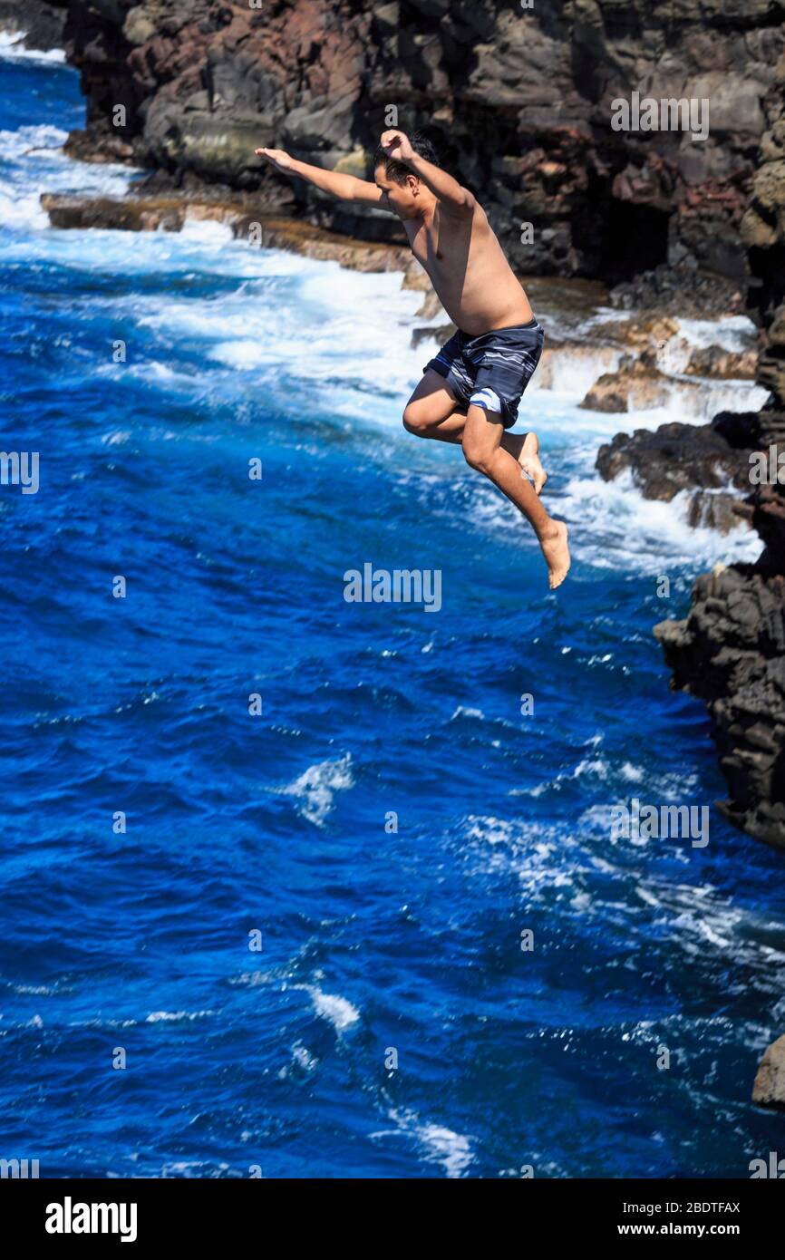 Junger Mann (Model veröffentlicht) springt von Klippe in den Ozean bei South Point, Hawaii Stockfoto