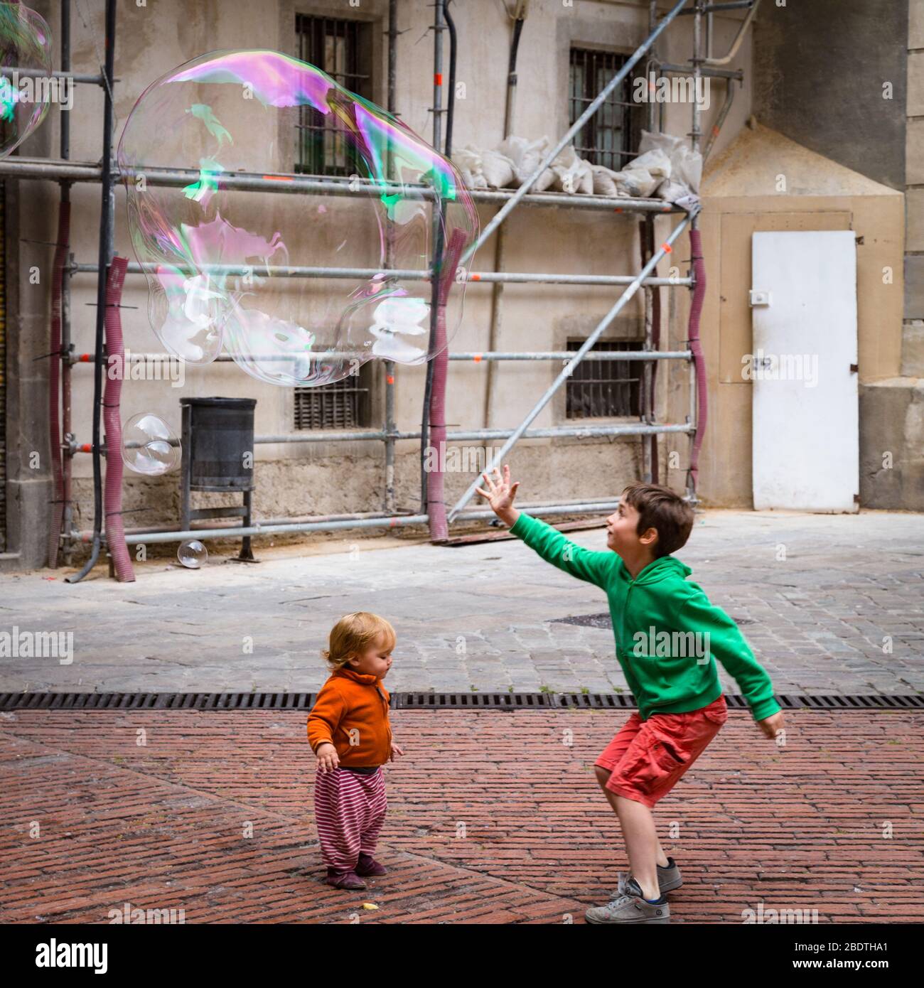 Zwei Kinder spielen mit Blasen auf einem kleinen Platz in Barcelona. Stockfoto