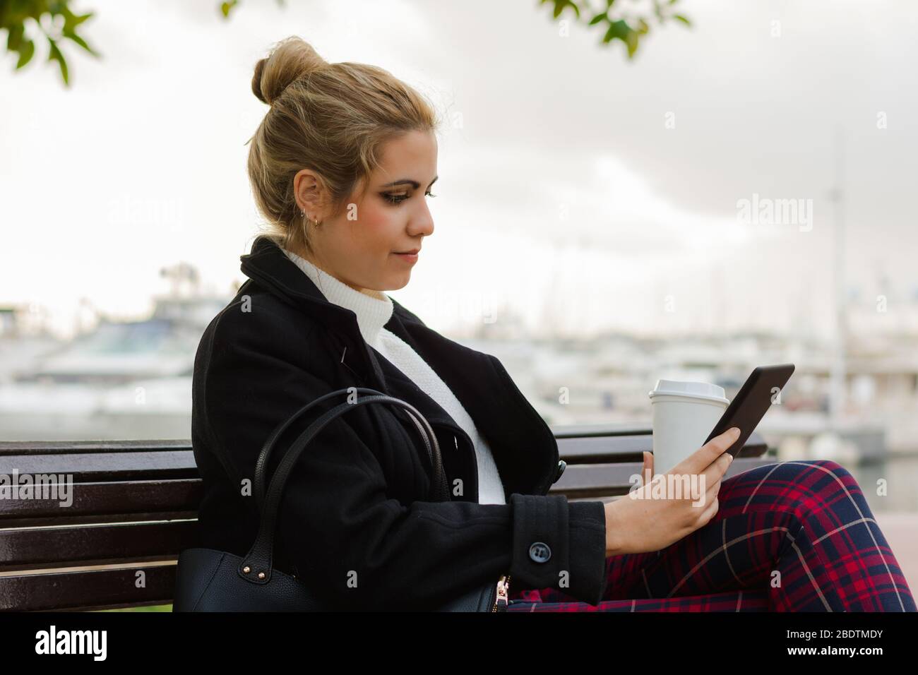 Junge Frau liest in ihrem elektronischen Buch auf einer Bank sitzen Stockfoto