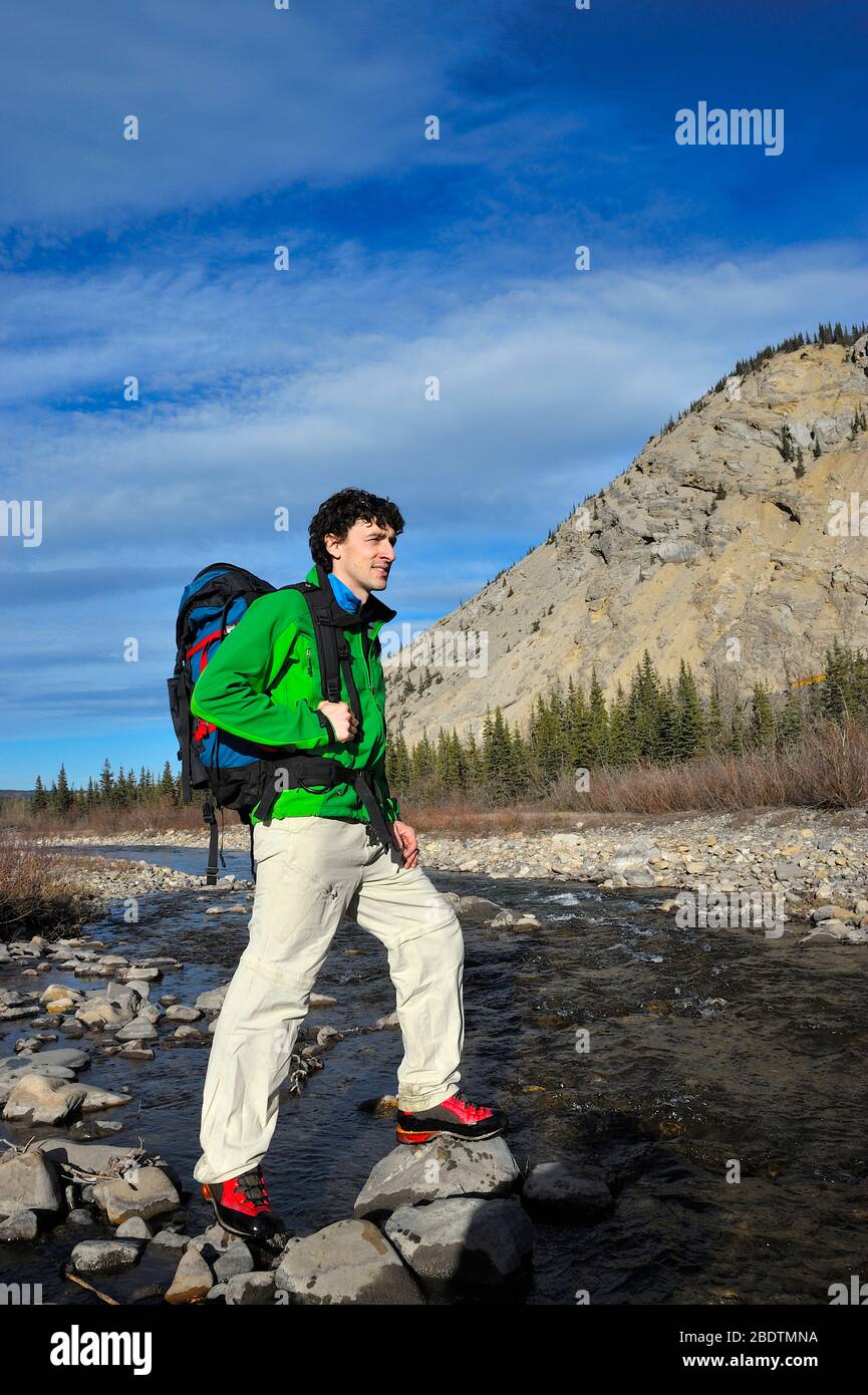 Ein einfarbiger, männlicher Wanderer, der einen Bach in den felsigen Bergen von Alberta Canada überquert Stockfoto