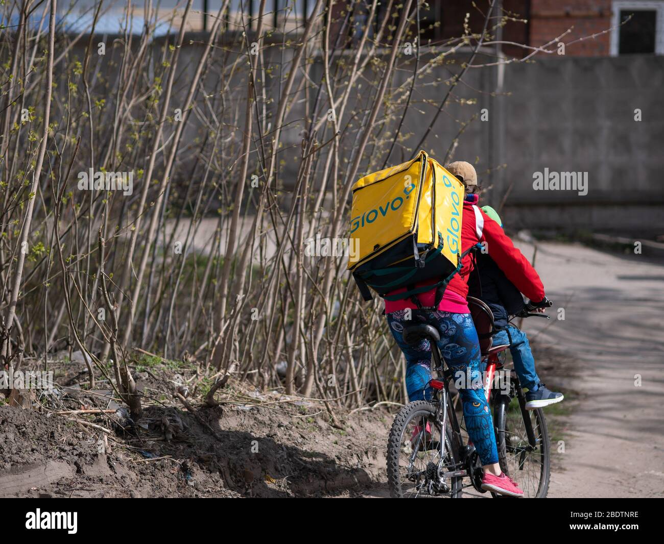 Dnipro, Ukraine - 27. März 2020: GLOVO Lieferung Frau Kurier auf Fahrrad mit Marken gelbe Thermorucksäcke liefern Kundenaufträge. Stadt wurde qu Stockfoto