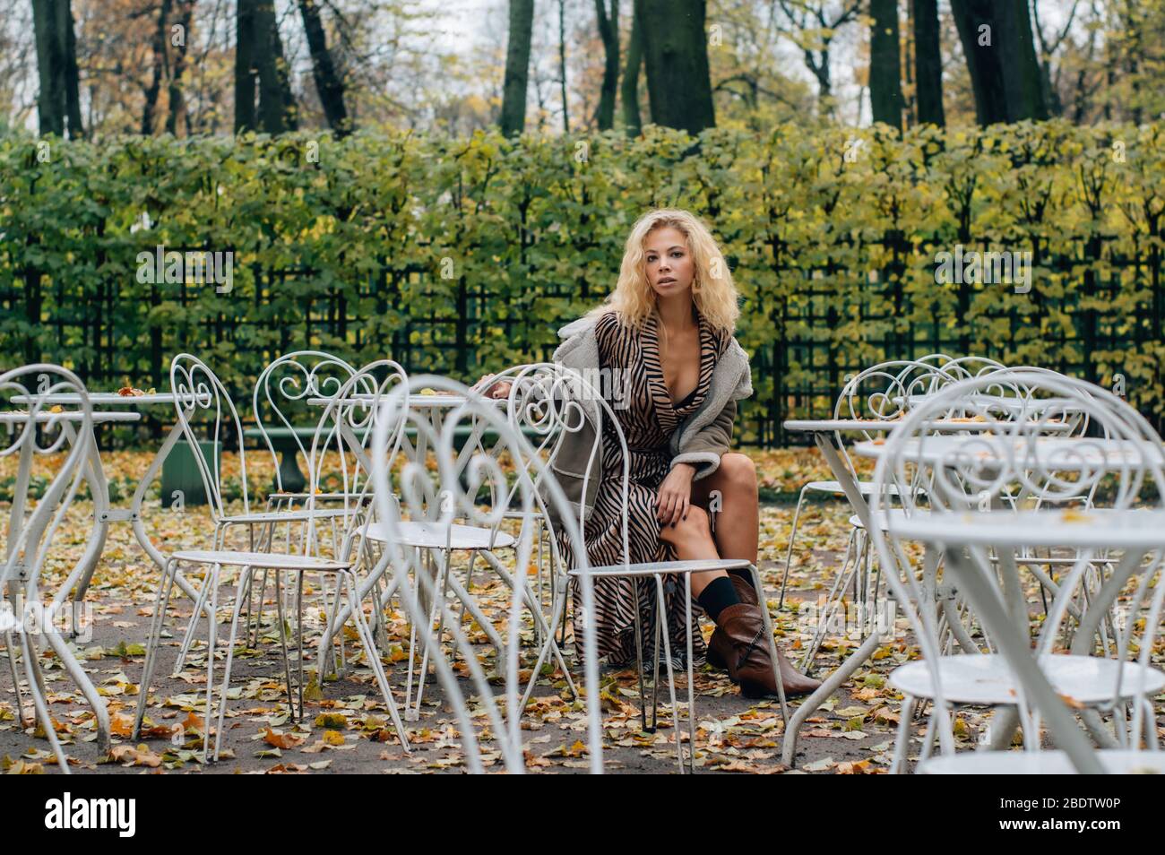 Junge blonde Mädchen sitzt am Tisch im öffentlichen Park im Herbst und schauen zu Kamera Stockfoto