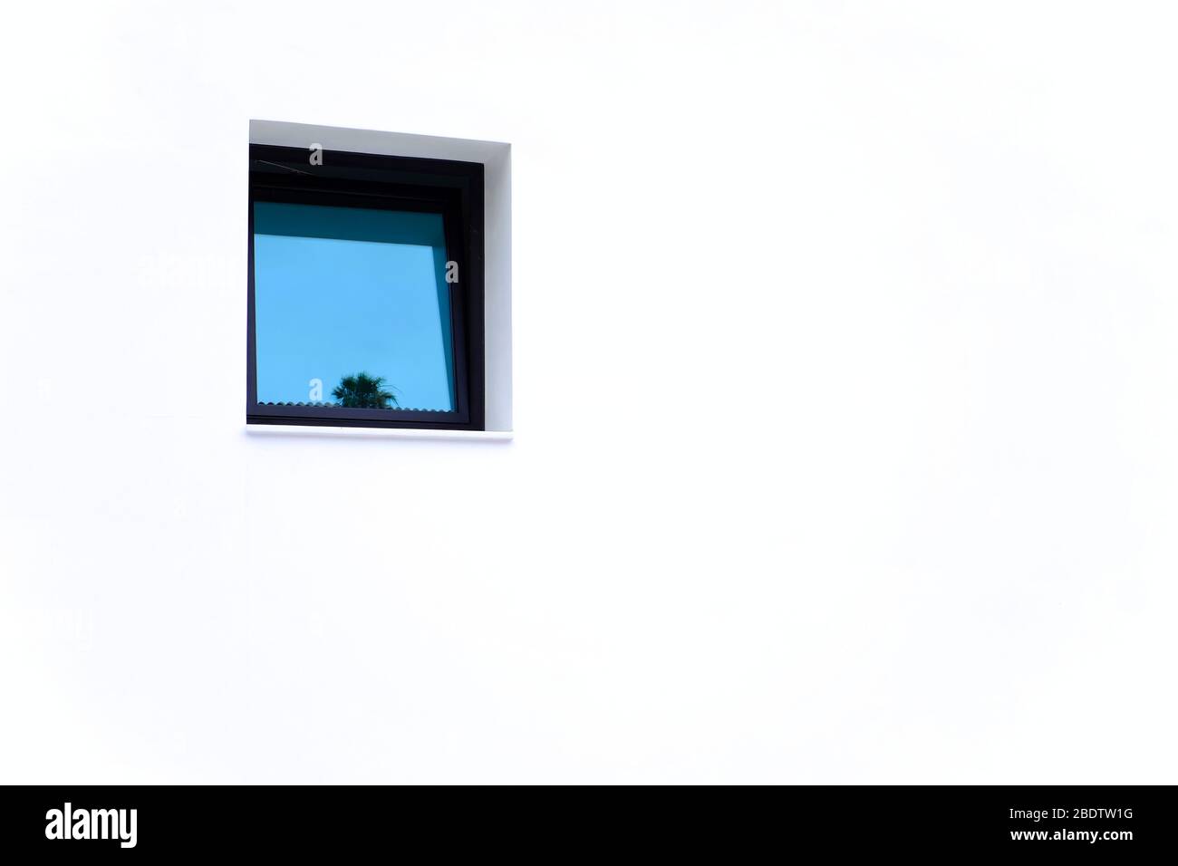 Ein kleines blaues Fenster mit einer Reflexion, helle weiße Wand, große Kopie / Text Raum. Stockfoto