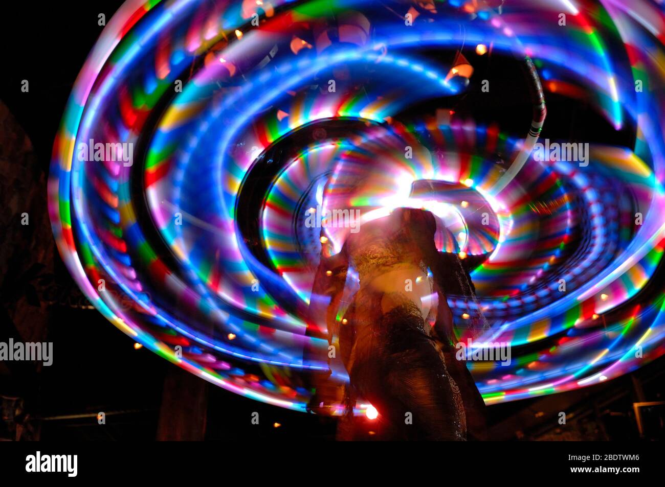 Tänzer mit mehrfarbigem Hula Hoop Reifen aufgenommen mit Slow Shutter Speed, um Bewegung und Weichzeichnung zu zeigen Stockfoto