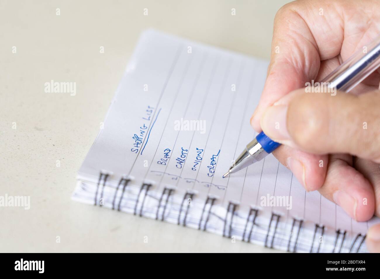 Ein Mann, der mit einem Stift eine Einkaufsliste auf einem Notizblock ausreitet Stockfoto