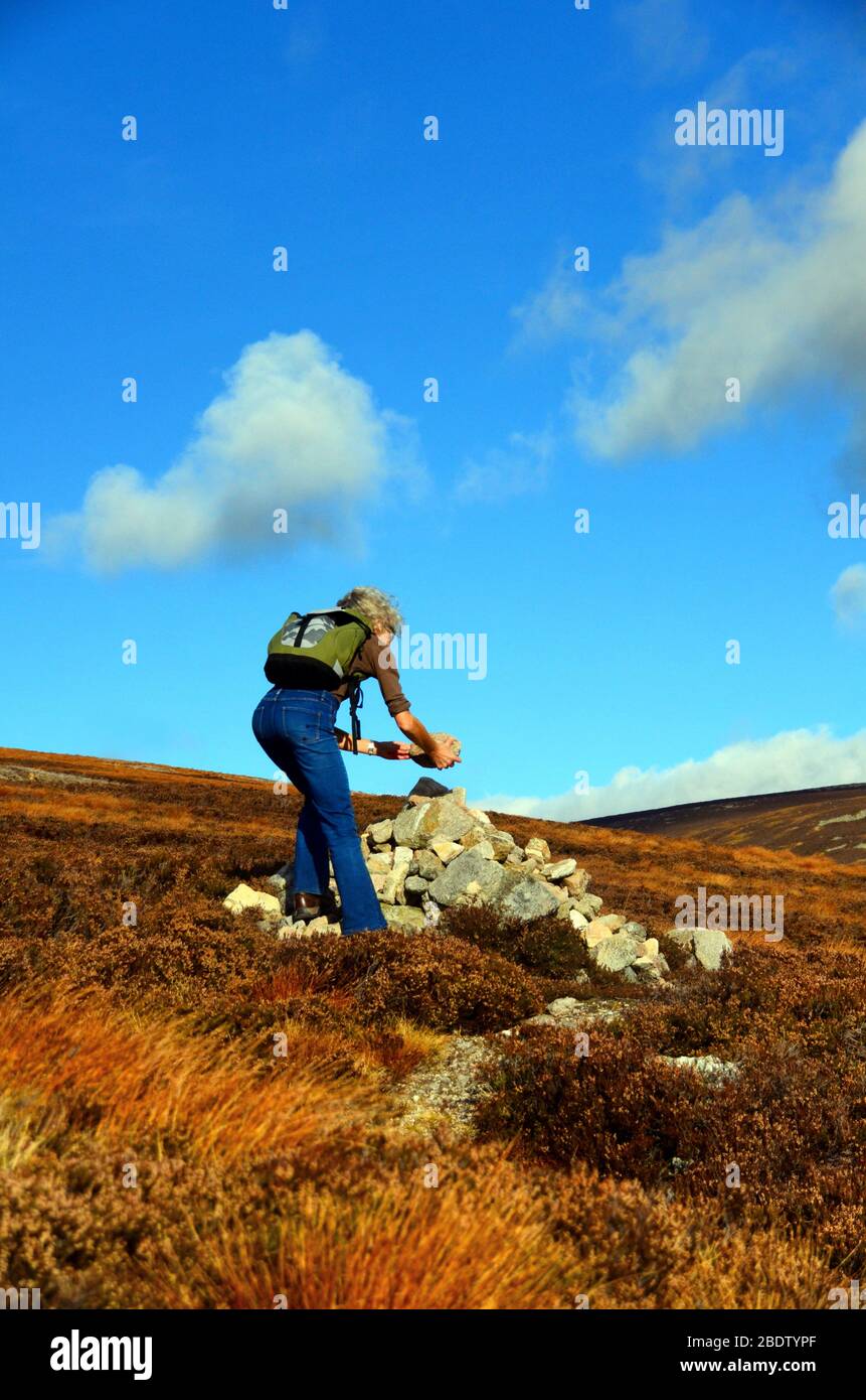 Eine Frau, die einen Felsen zu einem Kairn an der Seite eines Fußweges hinzufügt, der zum Gipfel des Mount Keen führt, in glen Esk Stockfoto