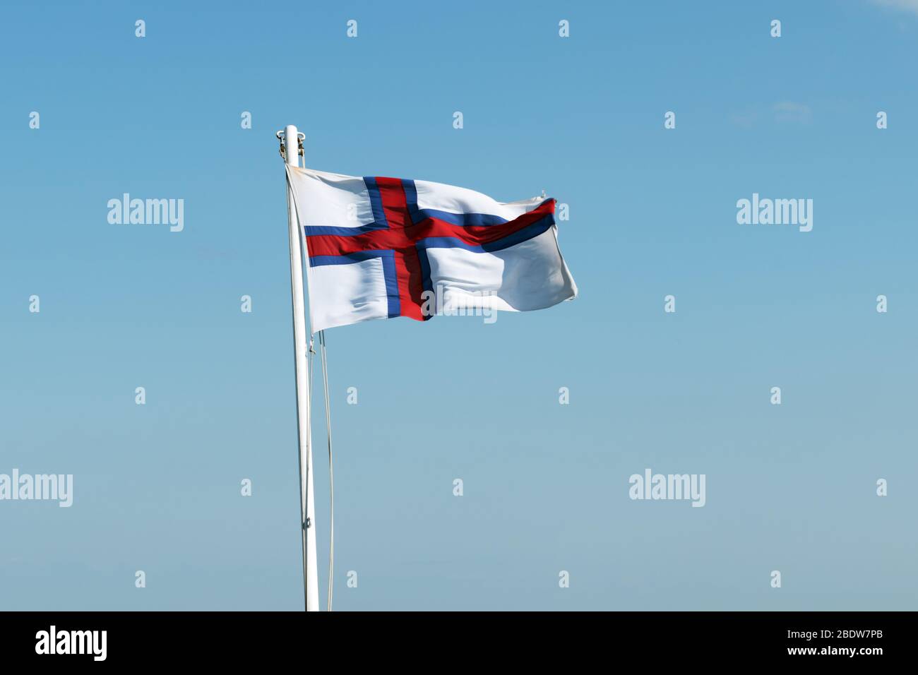 Flagge der Färöer Inseln winkt gegen einen klaren blauen Himmel Stockfoto