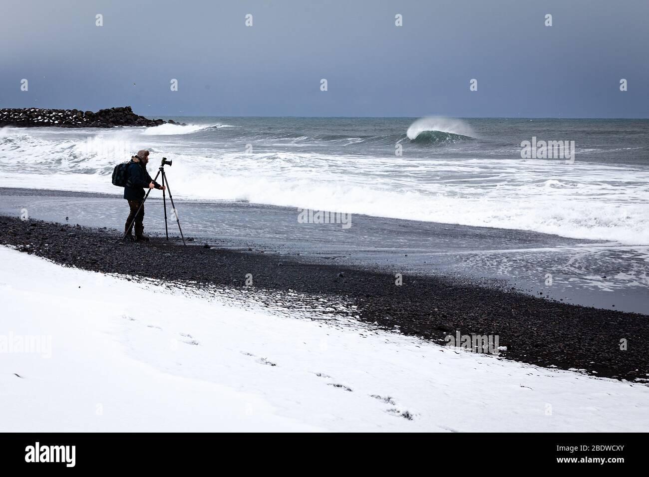 Ein Fotograf fotografiert das Meer am berühmten schwarzen Sandstrand Reynisfjara im Winter in Vík í Mýrdal an der Südküste Islands Stockfoto