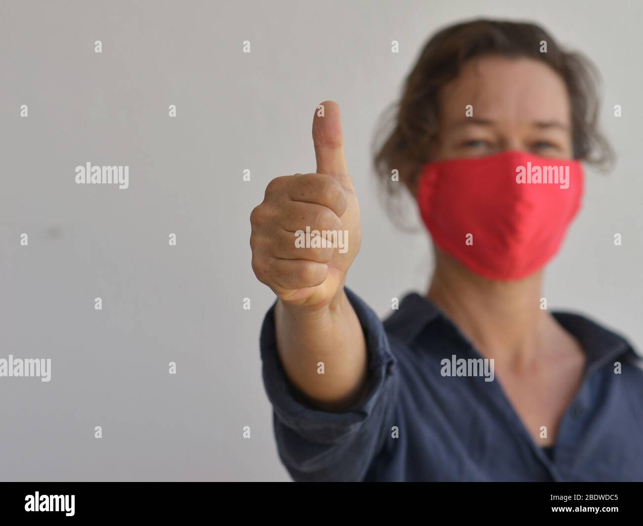 Kaukasierin trägt eine hausgemachte DIY Gesichtsmaske und gibt die Daumen-up-Zeichen während der 2019-20 Corona-Virus Pandemie. Stockfoto