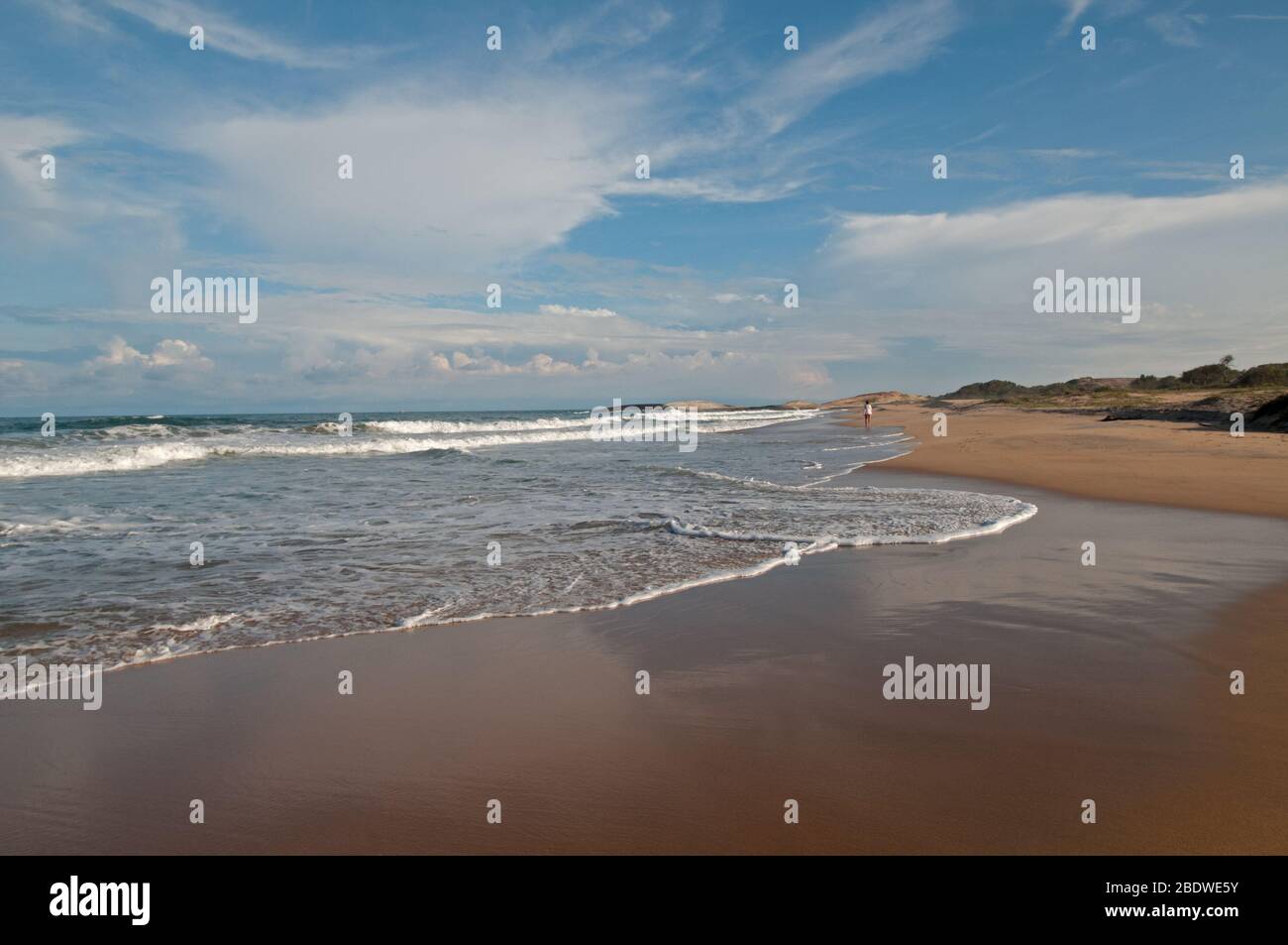 Dies ist ein Strand am Meer. Die Größe des Strandes, die Weite des Ozeans werden durch kleine Figur der Frau betont. Stockfoto