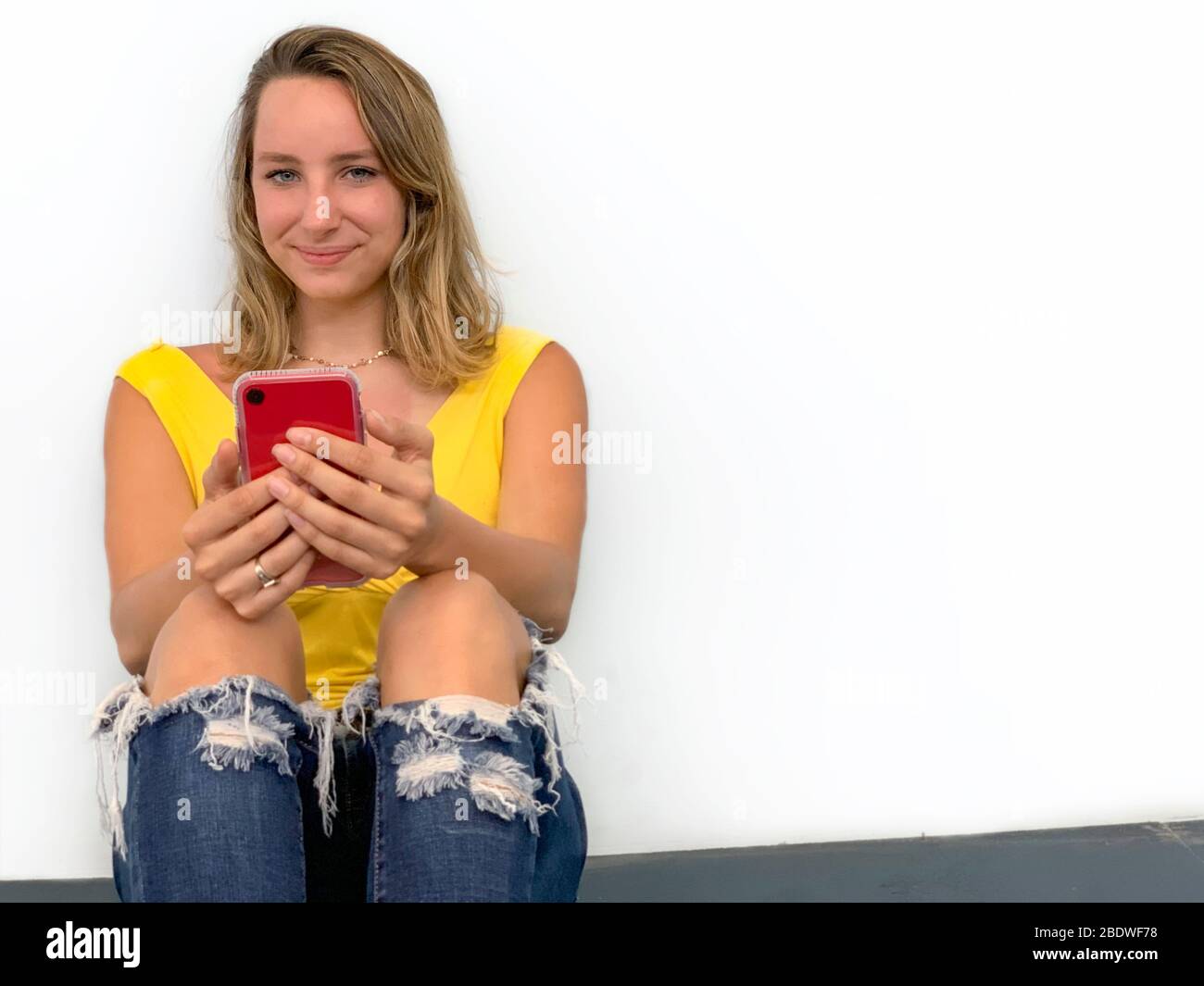 Porträt einer jungen Frau auf dem Boden mit Handy sitzen Stockfoto