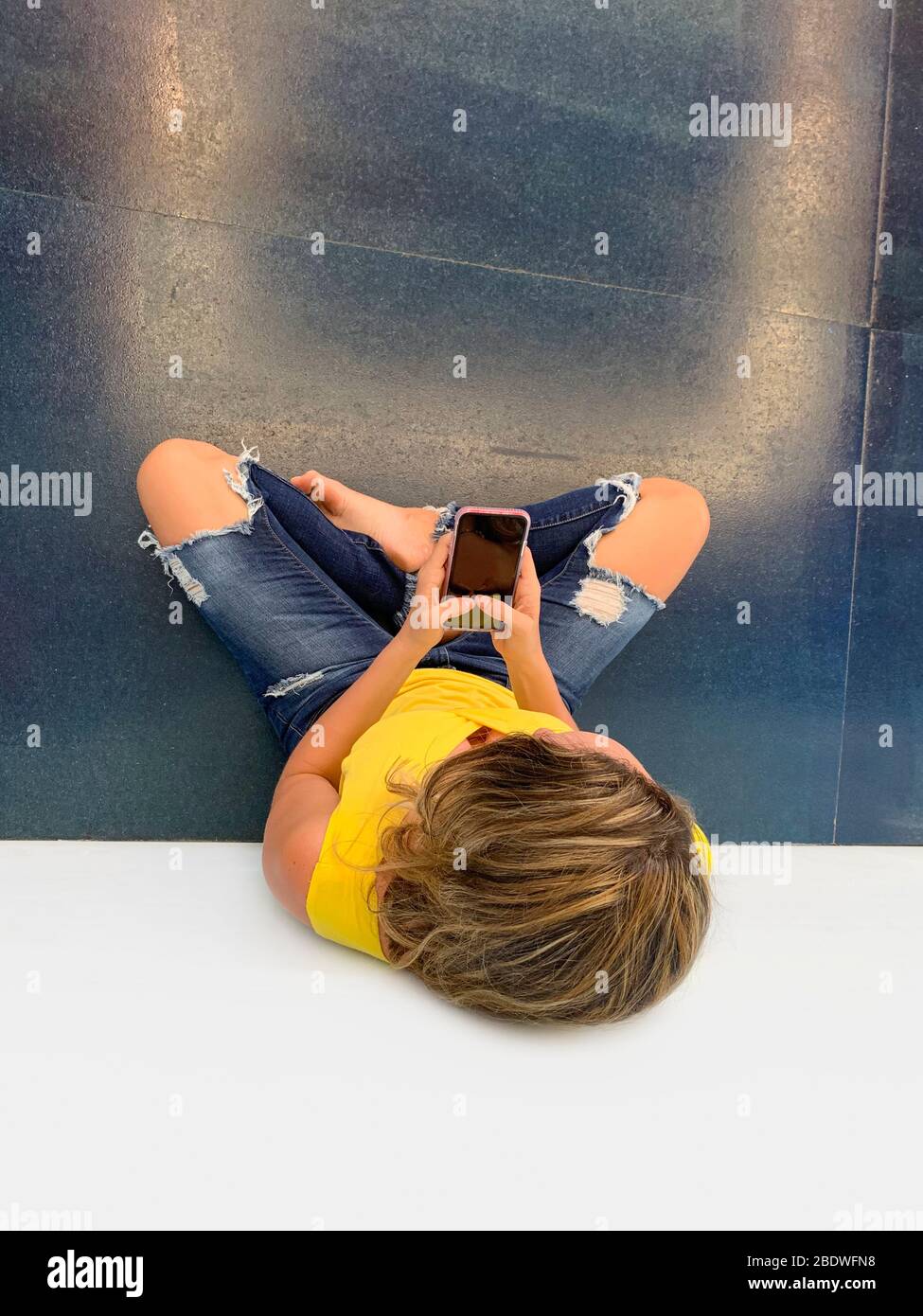 Porträt einer jungen Frau auf dem Boden mit Handy sitzen Stockfoto
