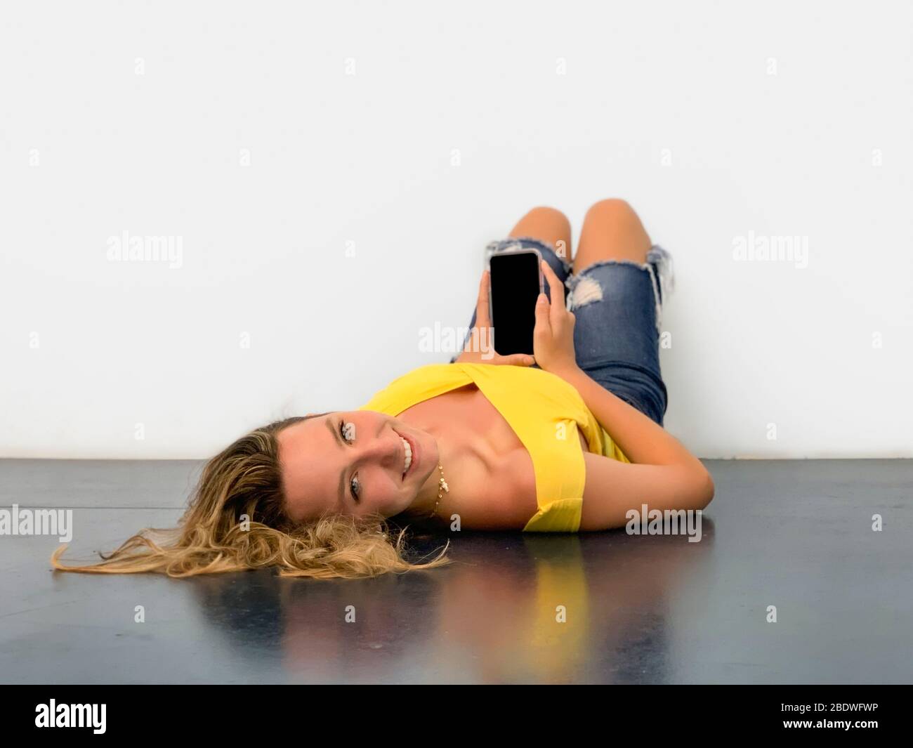 Junge Frau auf dem Boden mit Handy liegen Stockfoto