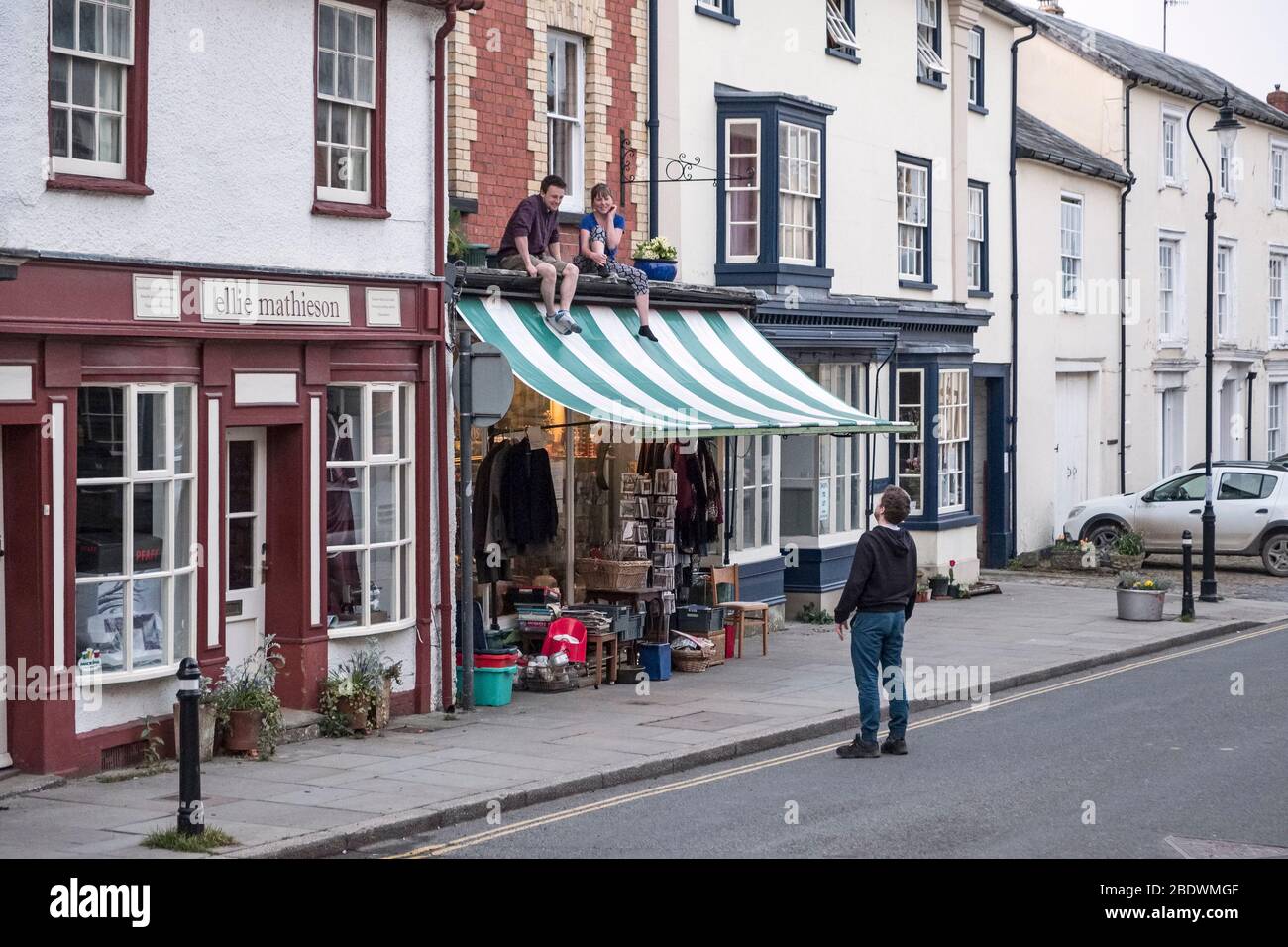 Freunde, die soziale Distanz von einem Vorsprung vor ihrer Wohnung im ersten Stock in der kleinen walisischen Stadt Presteigne, Powys, Wales, Großbritannien, aufrechterhalten Stockfoto