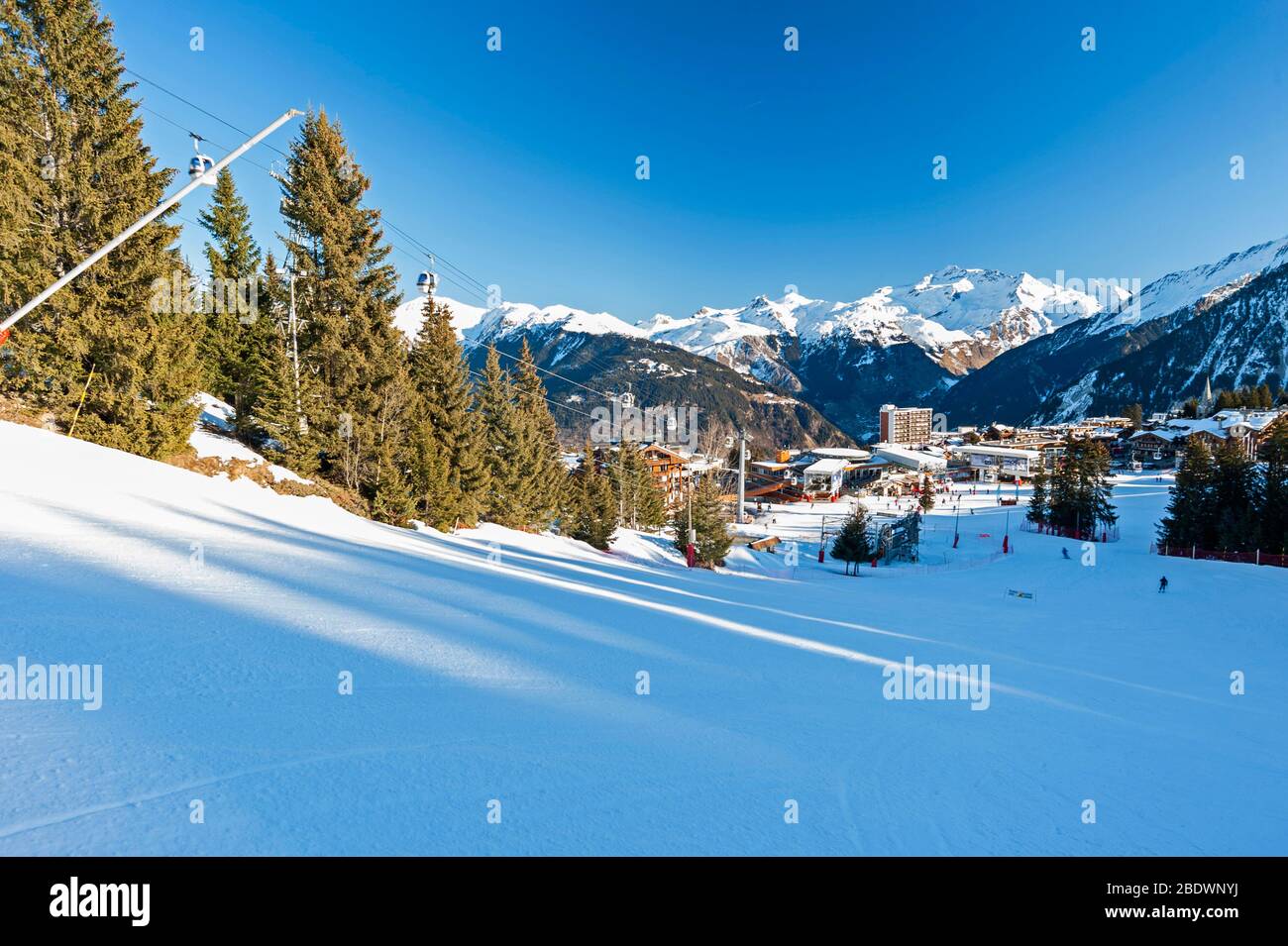 Blick hinunter eine Skipiste im Winter alpinen Bergort mit Dorf im Hintergrund Stockfoto