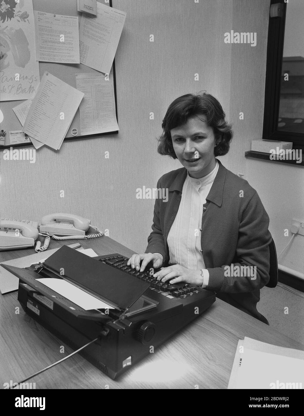 1987, eine Sekretärin an ihrem Schreibtisch mit einer modernen Schreibmaschine, einer elektronischen Schreibmaschine von 'Bruder' einer japanischen Firma. Brother Industries Wurzeln waren in der Nähmaschinenherstellung, und in den 1960er Jahren traten sie mit ihrer ersten tragbaren Schreibmaschine in den Markt für Bürogeräte ein, nachdem sie die britische Firma, die Jones Nähmaschinenfirma Co, ein Manchester-Geschäft, übernommen hatten. In den 1980er Jahren produzierten sie ihre erste elektronische Schreibmaschine und wurden zu einem von vielen japanischen Unternehmen, die große Produktionsstandorte in Großbritannien bauten. Stockfoto