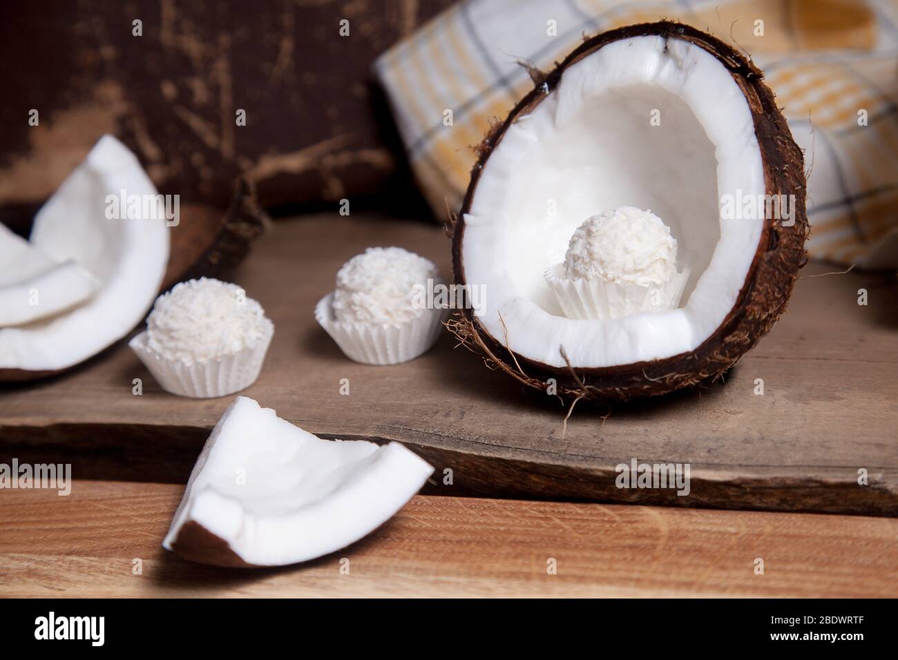 Kokosnuss- und süße Schokoladentrüffel. Kokosschale, Kokosflocken, kleine Stücke zerbroschter Nuss und weiße Kokosnussbonbons auf einem Woode Stockfoto