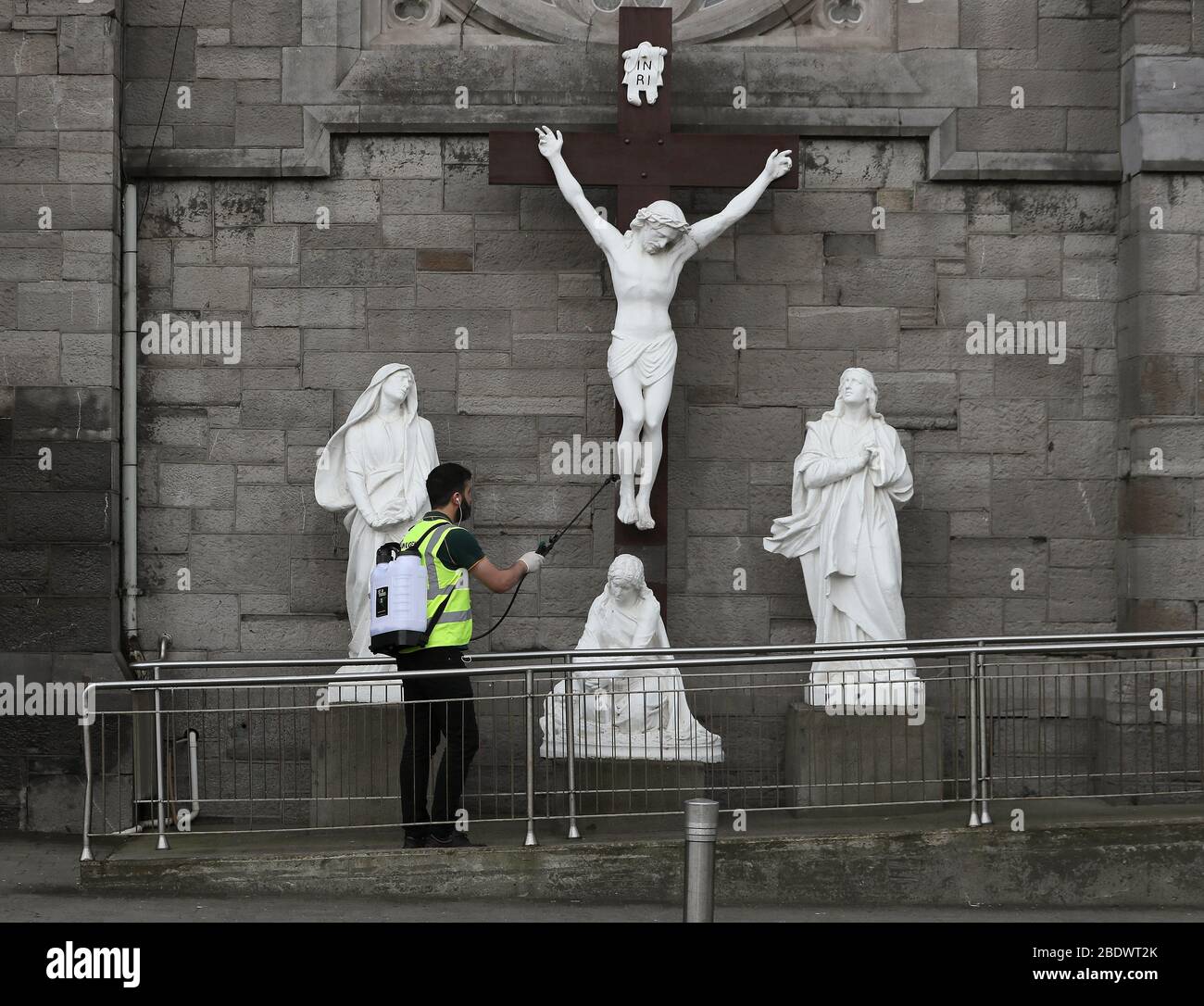 Ein Mann sprüht Desinfektionsmittel auf eine Statue der Kreuzigung Jesu vor der Kirche St. Maria der Engel in Dublin, am Karfreitag, dem christlichen Feiertag, der an die Kreuzigung Jesu und seinen Tod auf Golgatha erinnert. Stockfoto Ein Mann sprüht Desinfektionsmittel auf eine Statue der Kreuzigung Jesu vor der Kirche St. Maria der Engel in Dublin, am Karfreitag, dem christlichen Feiertag, der an die Kreuzigung Jesu und seinen Tod auf Golgatha erinnert. Stockfoto