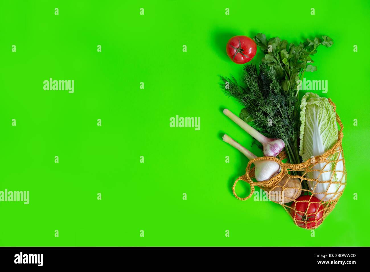 Aus einem gestrickten Beutel auf einem grünen Tisch werden Gemüse verstreut: Tomaten, Knoblauch, Kartoffeln, Chinakohl, Zwiebeln und ein Bündel Dill. Vegetarische Veg Stockfoto