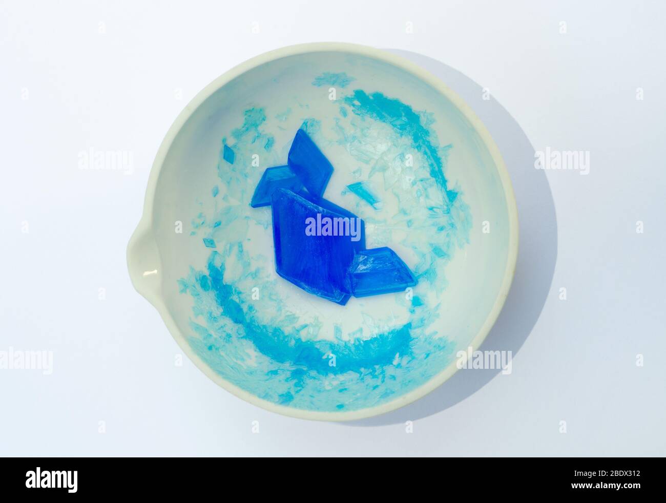 Ein weißes Porzellan-Verdampfungsbecken mit großen blauen Kupfersulfatkristallen auf weißem Hintergrund isoliert.die Kristalle wurden von Reacti produziert Stockfoto
