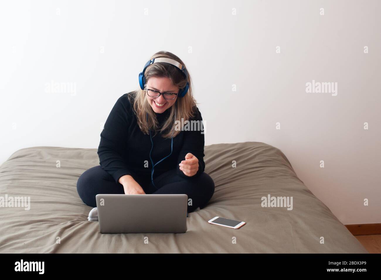 Glückliche Frau mit dem Computer in ihrem Schlafzimmer. Sie sitzt auf dem Bett und lächelt. Stockfoto