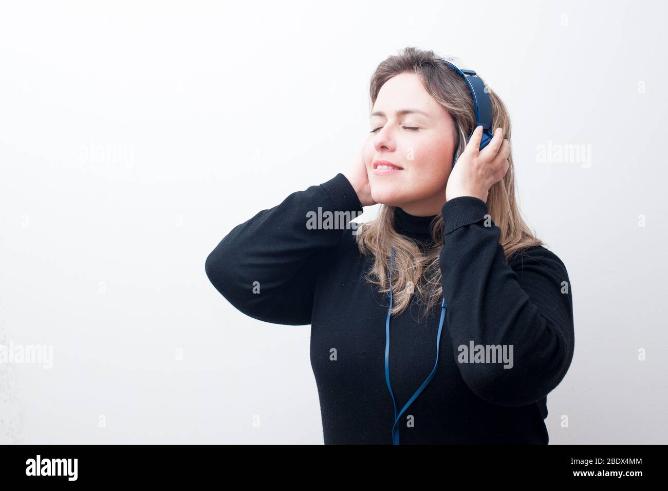 Blonde Frau, die mit ihren Händen auf dem Kopfhörer in einem weißen Hintergrund Musik hört. Großer Kopierplatz. Stockfoto