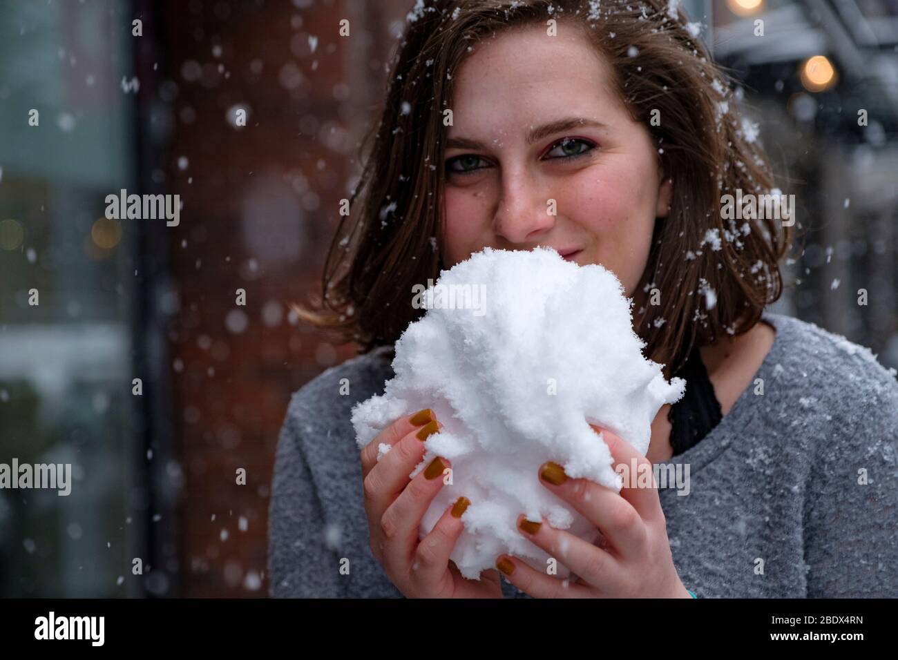 Ein junges, schönes Mädchen isst Schnee. Sie möchte ein Gehirngefrieren bekommen. Stockfoto