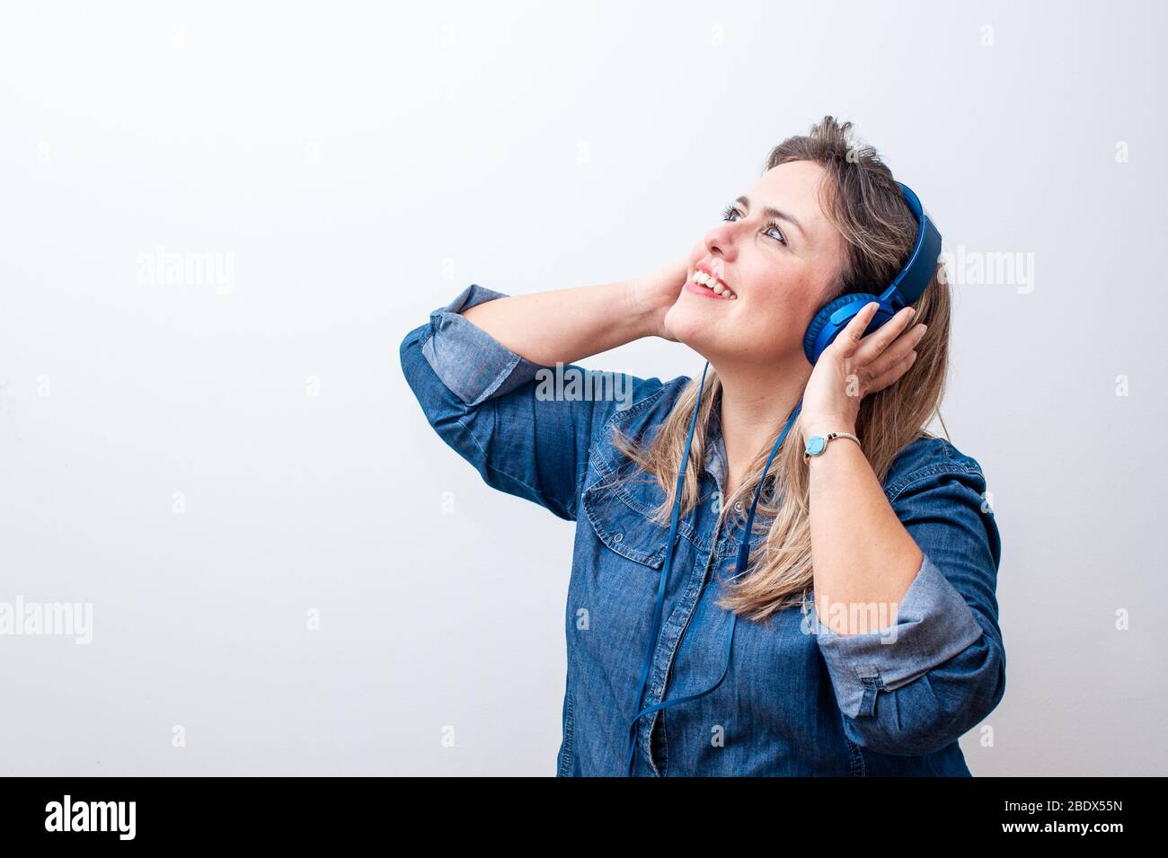 Glückliche blonde Frau, die Musik mit ihren Händen auf dem Kopfhörer in einem weißen Hintergrund hört. Großer Kopierplatz. Stockfoto