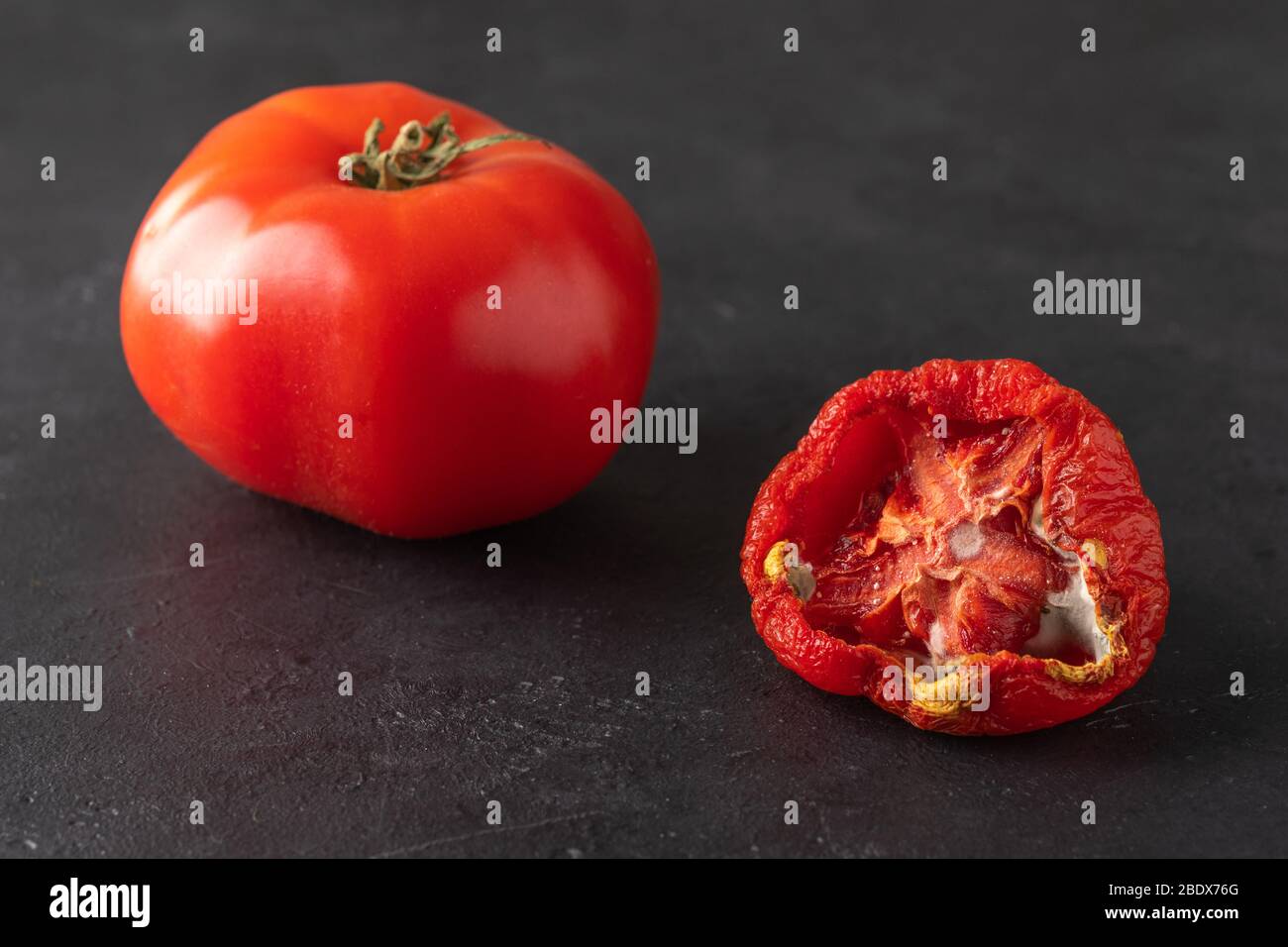 Verdorbene und frische Tomaten auf schwarzem Hintergrund. Tomate mit Schimmel. Unsachgemäße Lagerung von Gemüse. Verschwenden Sie Lebensmittel. Nahaufnahme Stockfoto