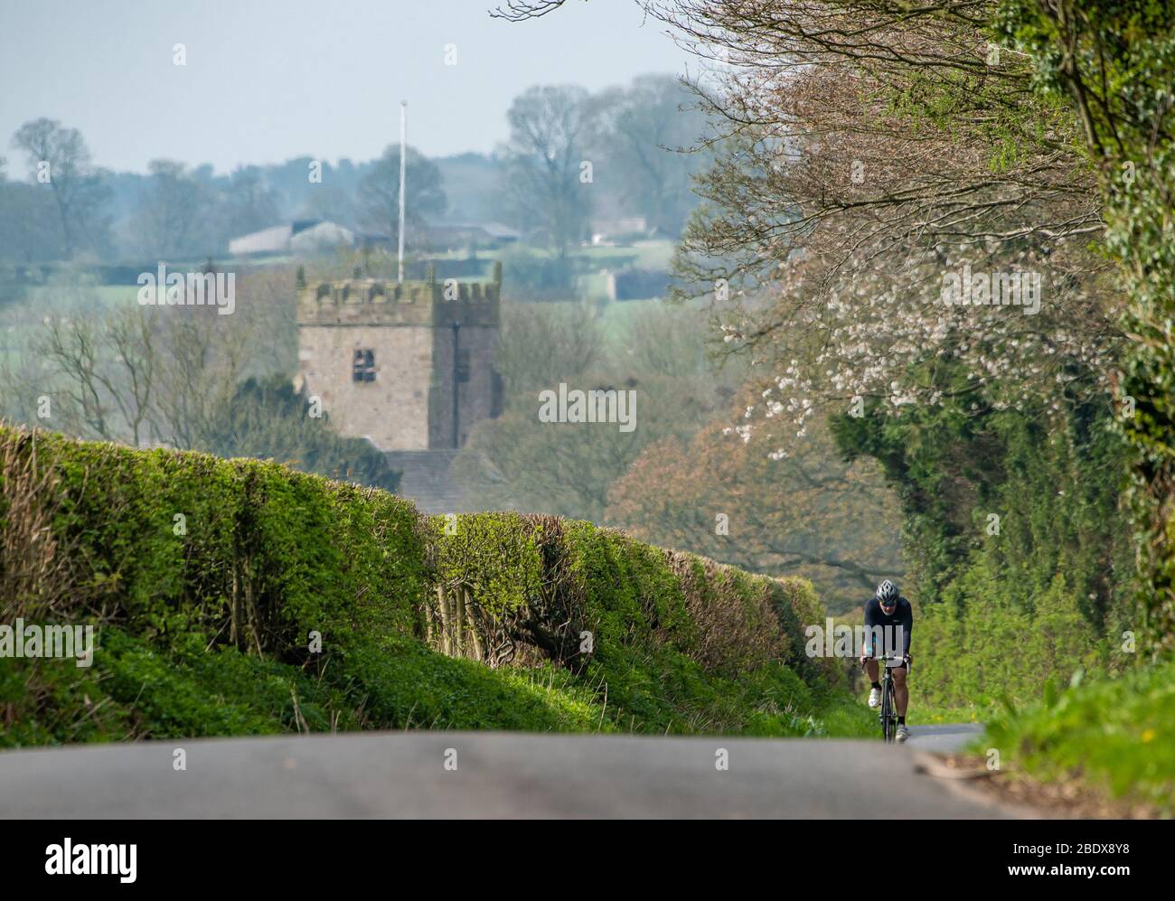 Preston, Lancashire, Großbritannien. April 2020. Ein schöner Tag als Radfahrer genießt seine tägliche Übung auf den Landstraßen in der Nähe von Chipping, Preston, Lancashire mit St. Bartholomews Kirche im Hintergrund für Gottesdienst über das Osterwochenende geschlossen. Quelle: John Eveson / Alamy Live News Stockfoto