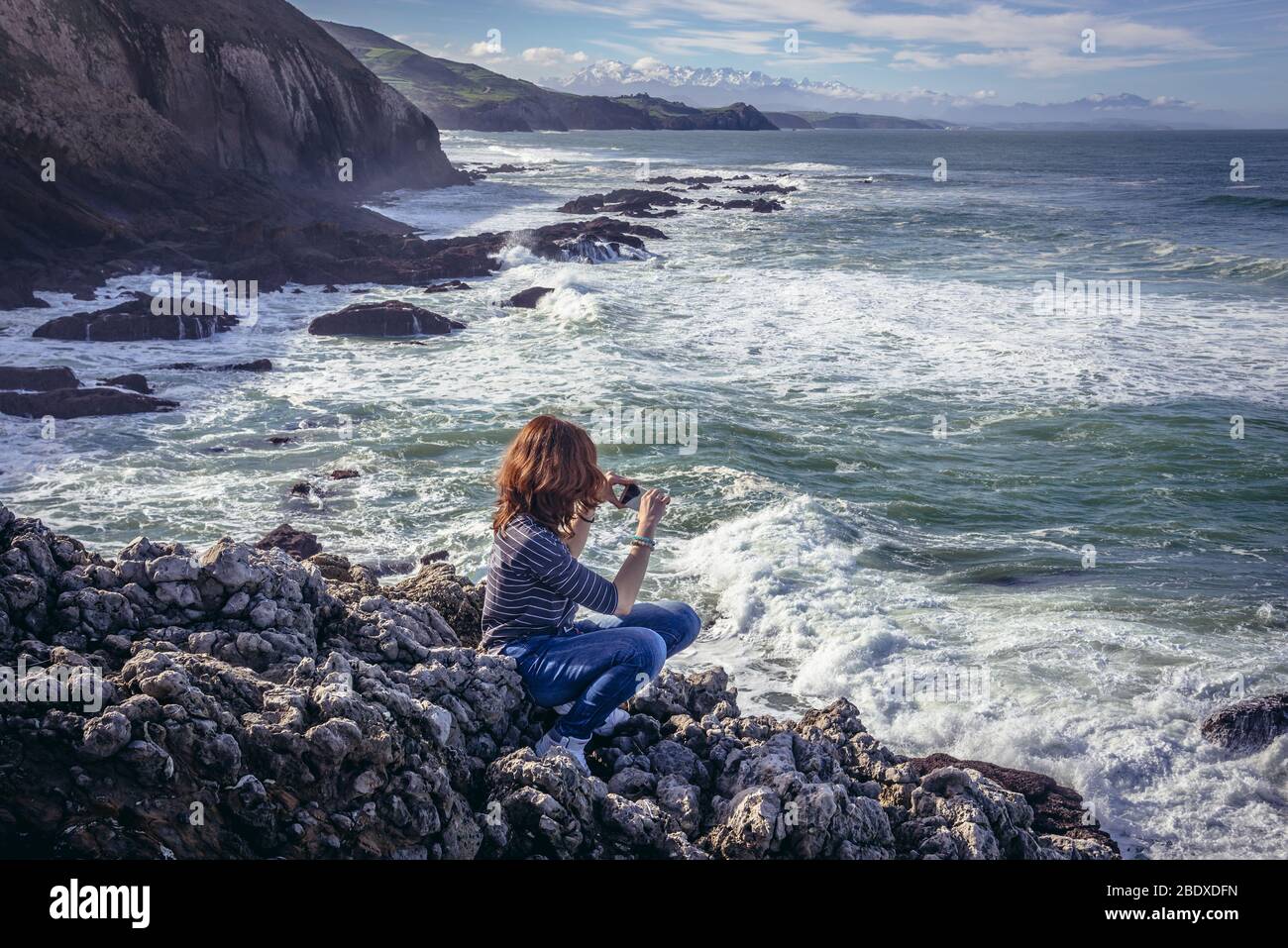 Tourist auf einem Felsen über dem Atlantischen Ozean in der Nähe von Strand von Santa Justa in Ubiarco Dorf. Gemeinde Santillana del Mar, Spanien Stockfoto