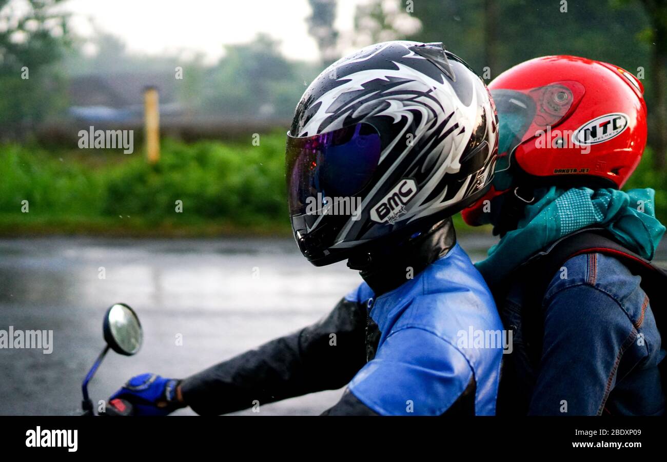 Zwei Personen, die ein Motorrad mit Helmen fahren, Sicherheitsmaßnahmen auf der Straße, ein Fahrzeug bei Regenwetter fahren Stockfoto