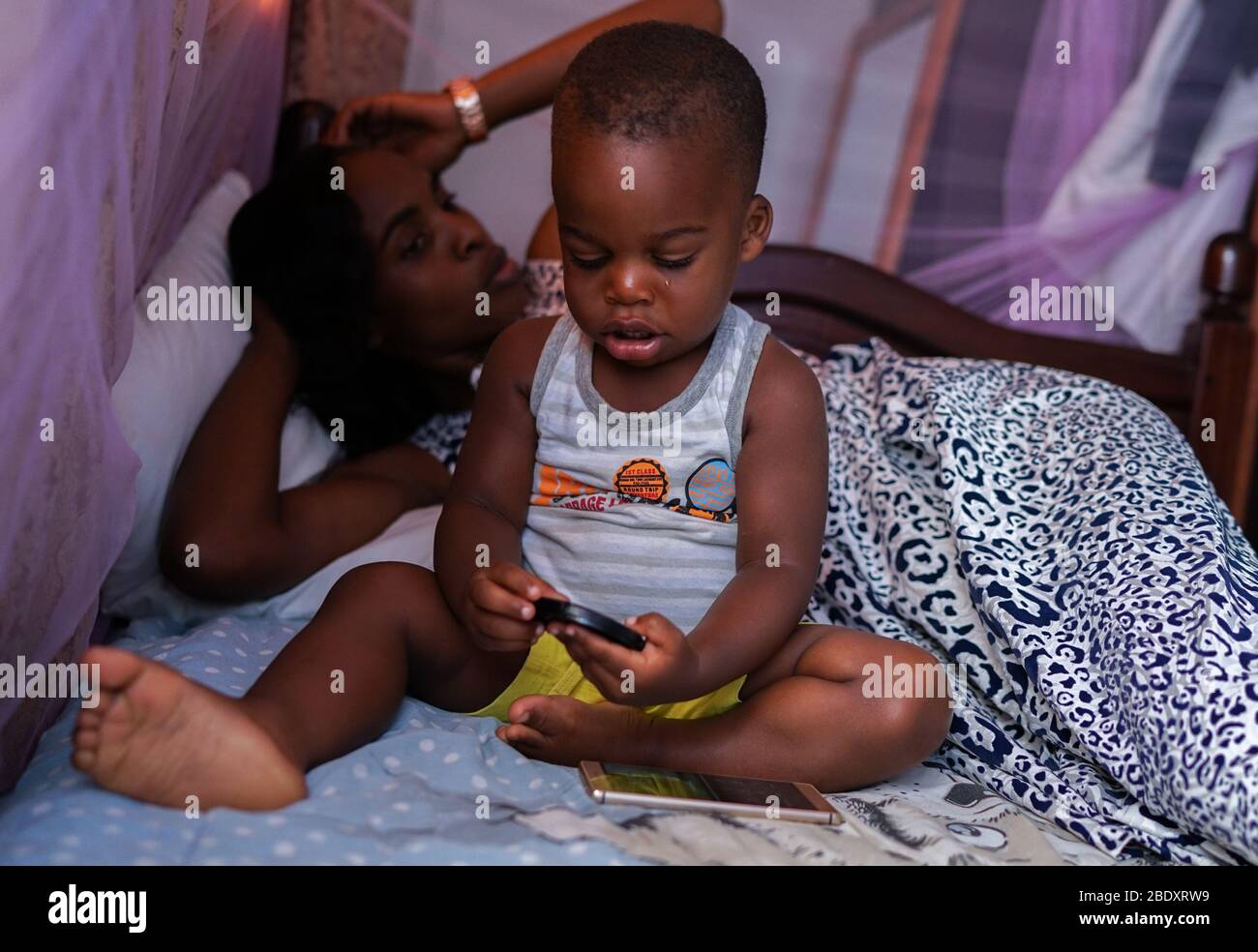 Kampala, Uganda - 15th. Juni 2017: Ein Porträt einer Afrikanerin mit ihrem Sohn, während sie am Nachmittag im Schlafzimmer auf einem Bett ruhten Stockfoto