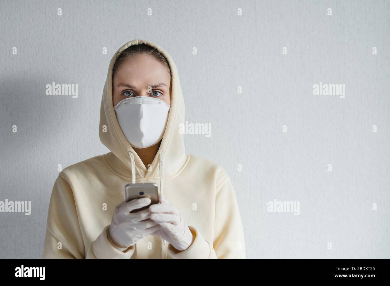 Eine junge Frau in medizinischer Maske im Gesicht nutzt das Smartphone. Stockfoto