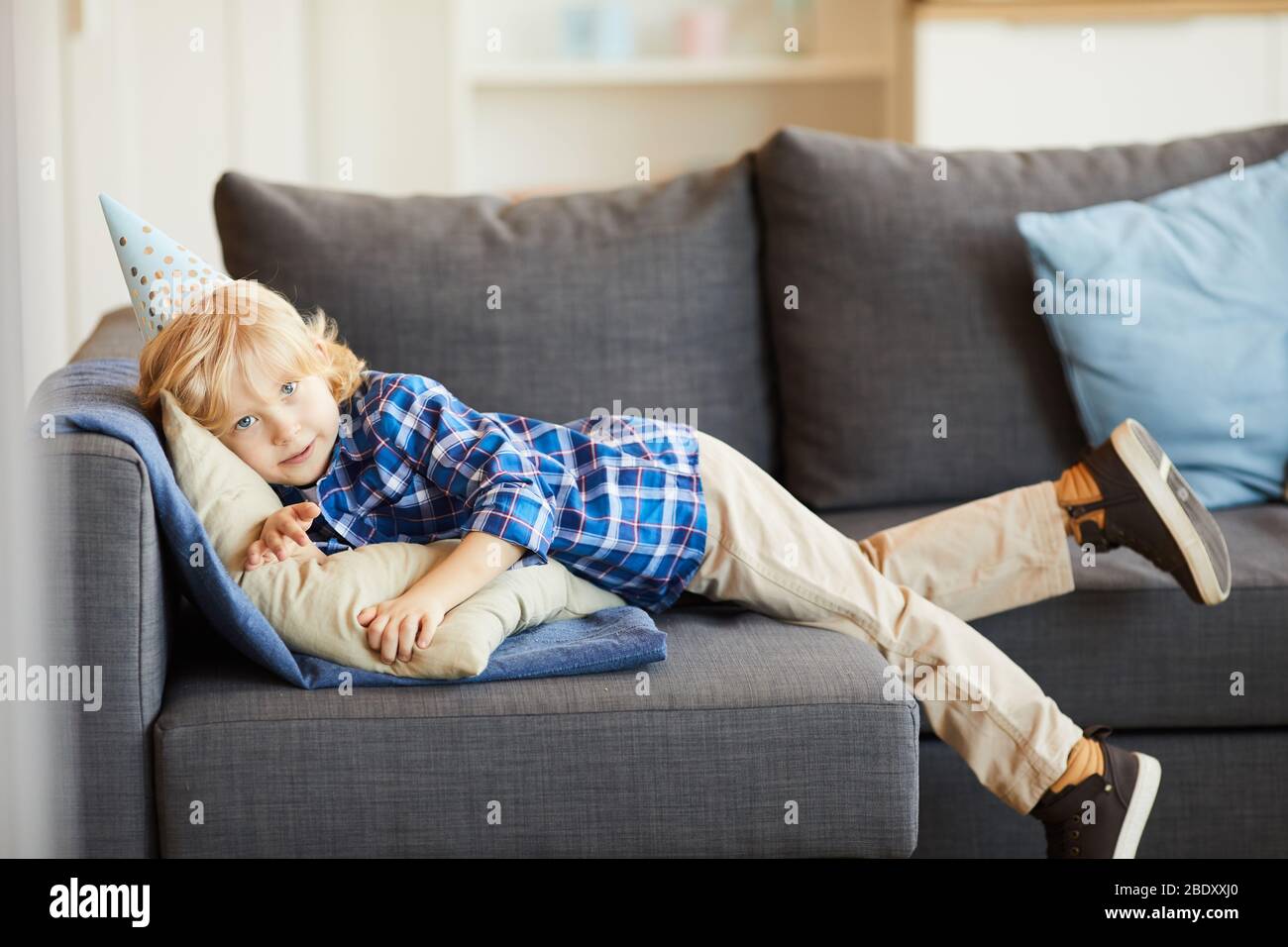 Portrait des kleinen Jungen in lässiger Kleidung, der auf dem Sofa liegt und sich zuhause im Wohnzimmer ausruht Stockfoto