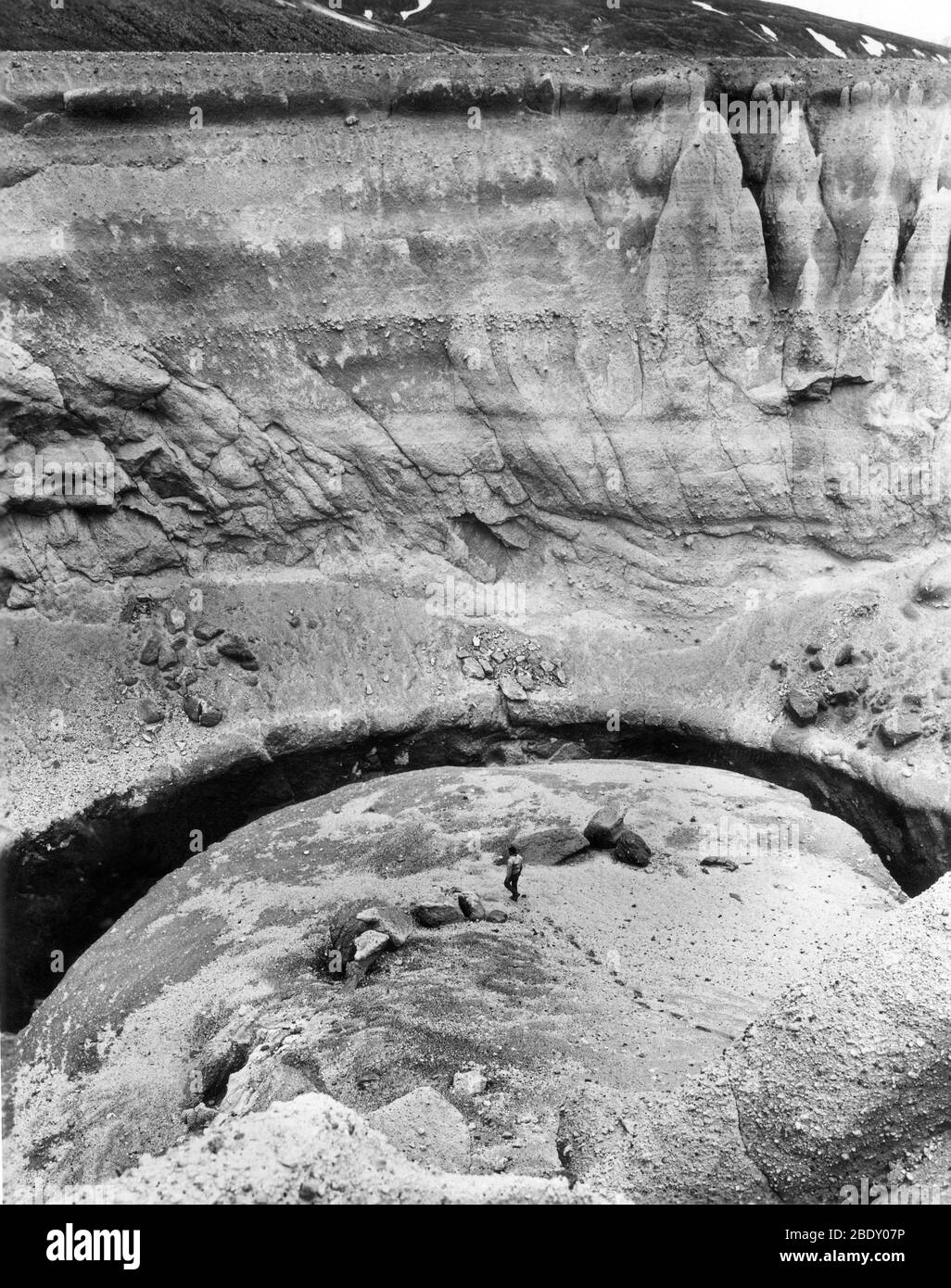 Klippen aus Vulkanasche und Bimsstein ragen über einem Geologen, der den Deep Creek Canyon im Sommer 1965 erkundet. Vulkanische Ablagerungen wurden während des Ausbruchs des Mt. Katmai im Jahr 1912. Das Katmai National Monument umfasst 2,697,590 Hektar und wurde 1918 gegründet. Die Gegend bietet mehrere aktive Vulkane Alaskas, einschließlich Mount Triton, und das berühmte Tal der 10,000 Raucher. Stockfoto