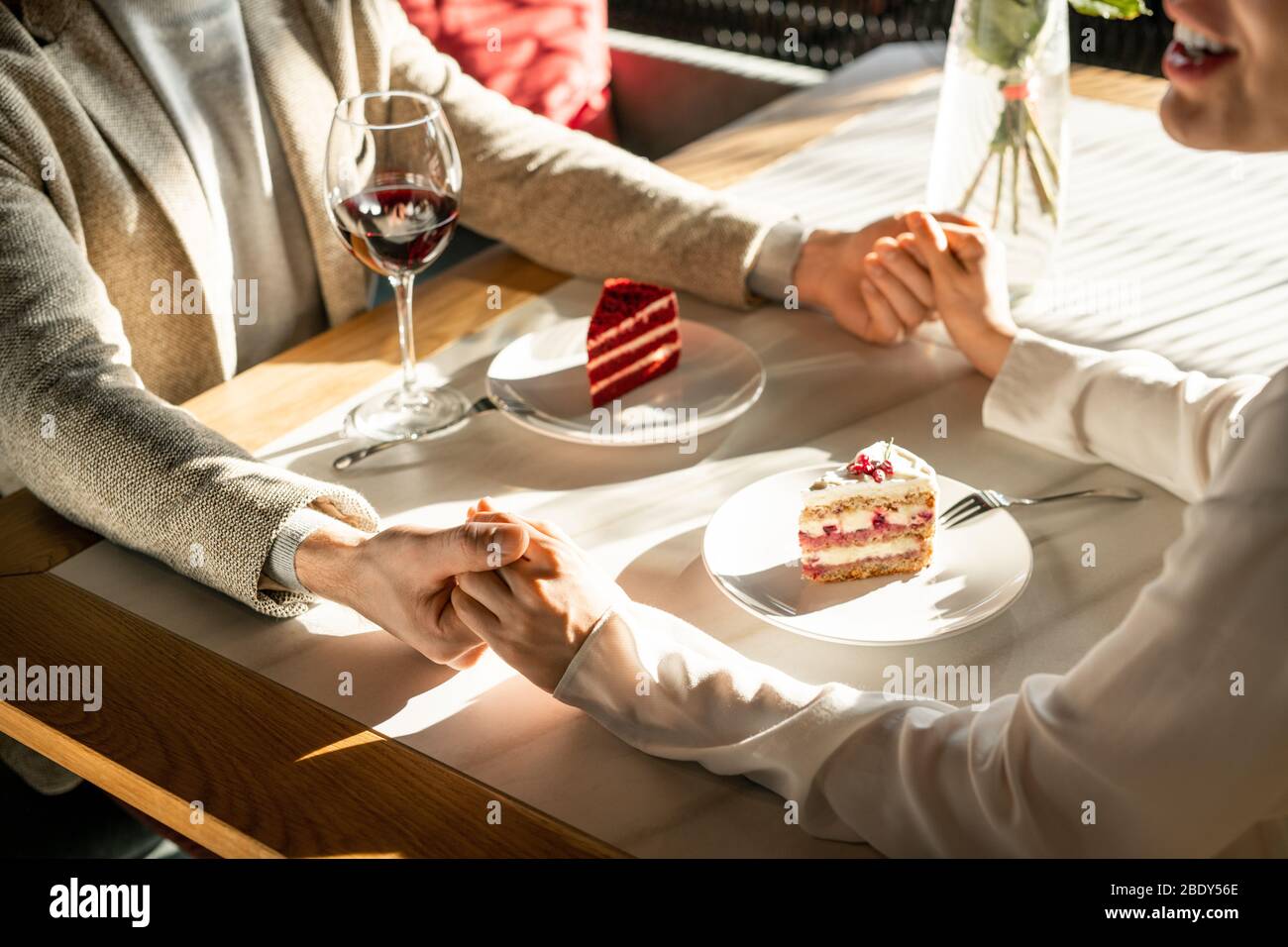Zwei junge romantische Datteln halten von Händen über servierten Tisch während leckere Kuchen und Rotwein nach dem Mittagessen in edlem Restaurant Stockfoto