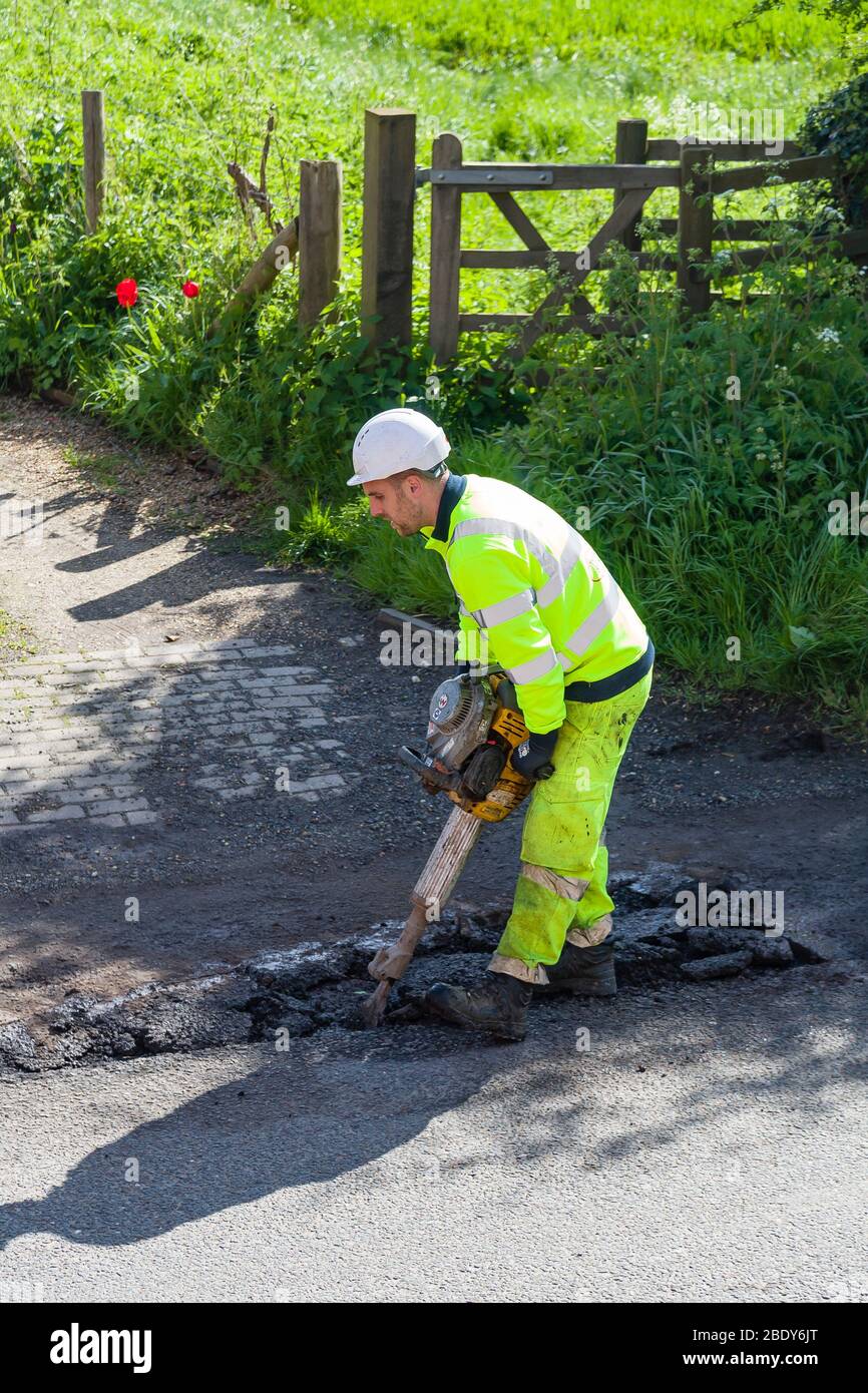 BUCKINGHAM, Großbritannien – 03. Mai 2018. Mann trägt gut sichtbare Kleidung, die Schlaglöcher auf beschädigter Fahrbahn repariert Stockfoto
