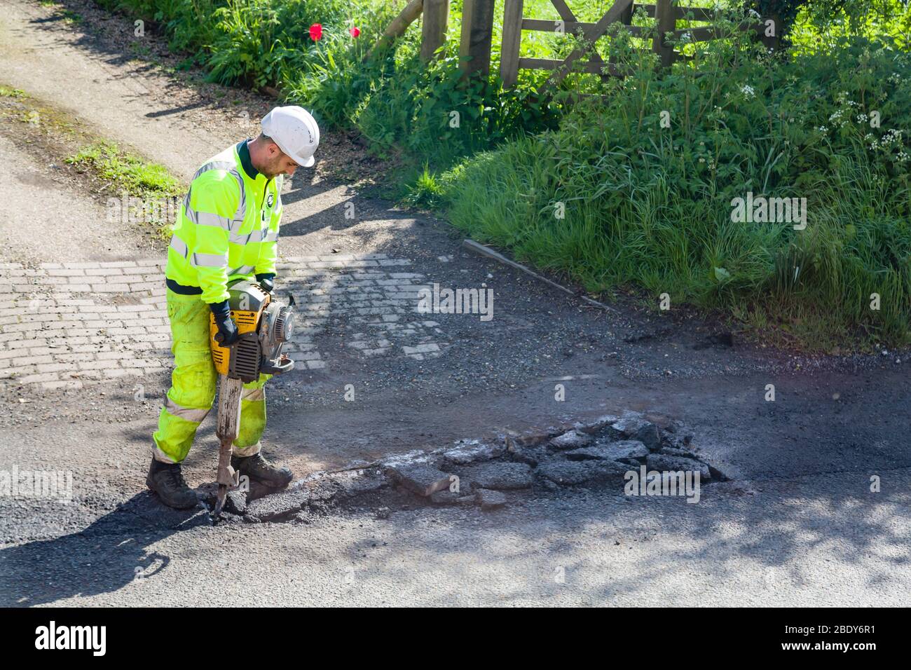BUCKINGHAM, Großbritannien – 03. Mai 2018. Straßenarbeiter, die gut sichtbare Kleidung tragen, reparieren Schlagloch auf beschädigter Straße Stockfoto