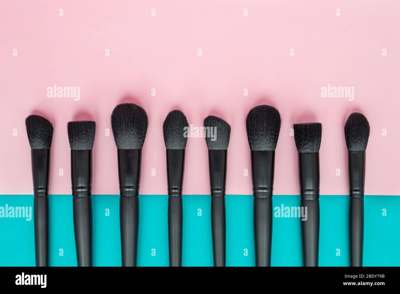 Flaches Lay von schwarzen Make-up-Bürsten auf einem rosa und blauen Hintergrund Stockfoto