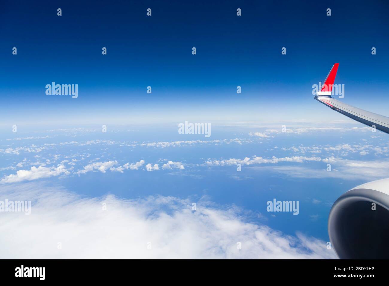 Blick aus dem Fenster des Flugzeugflügels und der Maschine über Wolken und Atlantik, mit blauem Himmel und Horizont. Zeigt Geschäftsreisen der Fluggesellschaft Stockfoto